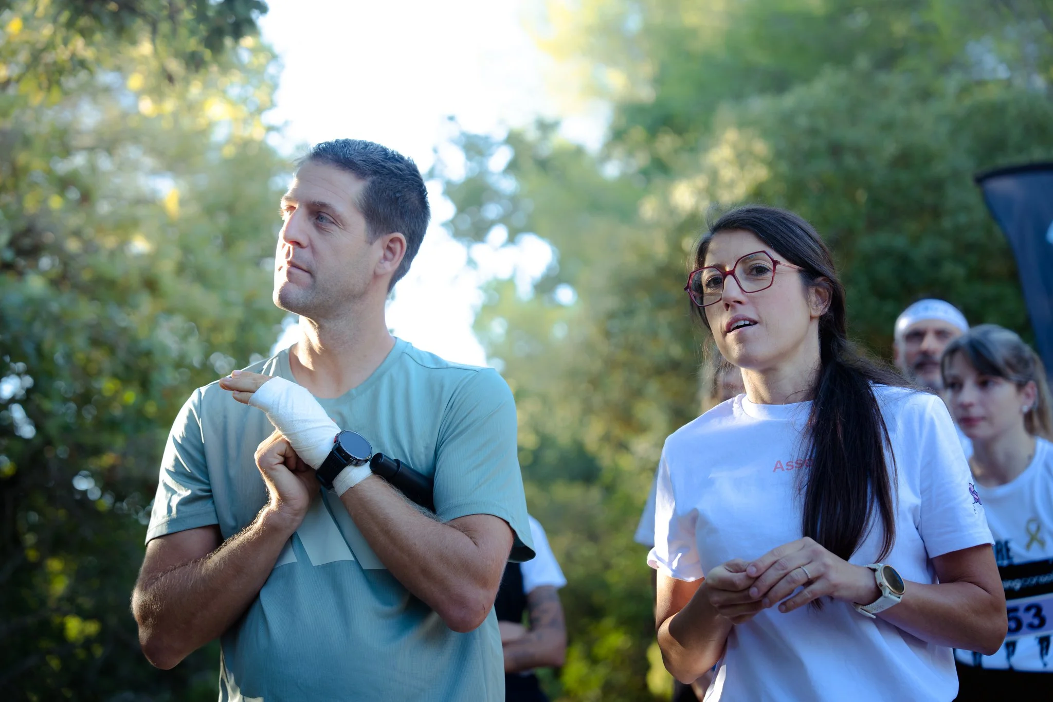 Des personnes participent à une course ou un événement en extérieur, avec un homme portant une montre et une femme portant des lunettes rouges, tous deux vêtus de vêtements de sport.