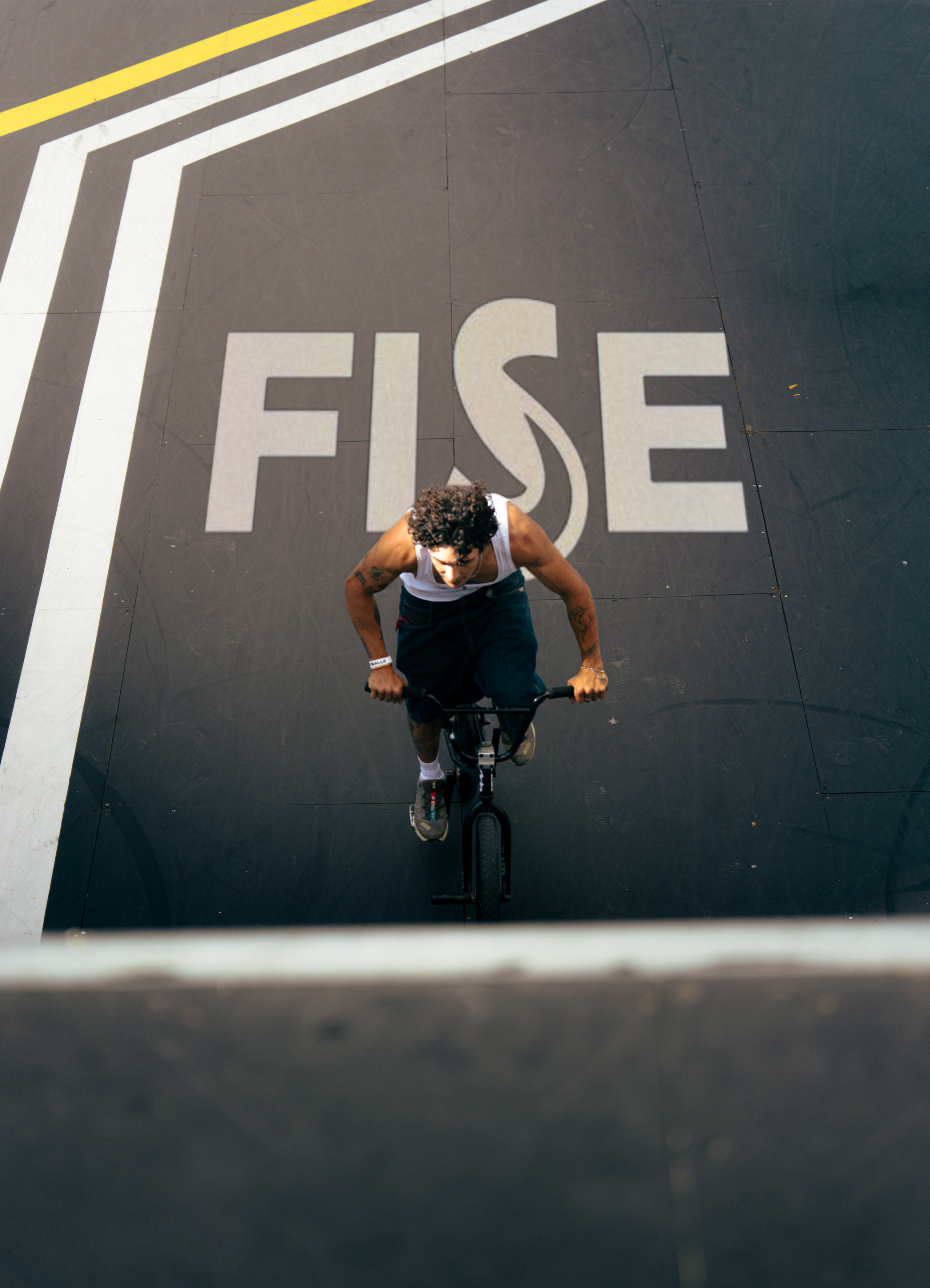 A person riding a bicycle on a black court with white and yellow lines, with the word 'FIRE' painted on the court surface, viewed from above.