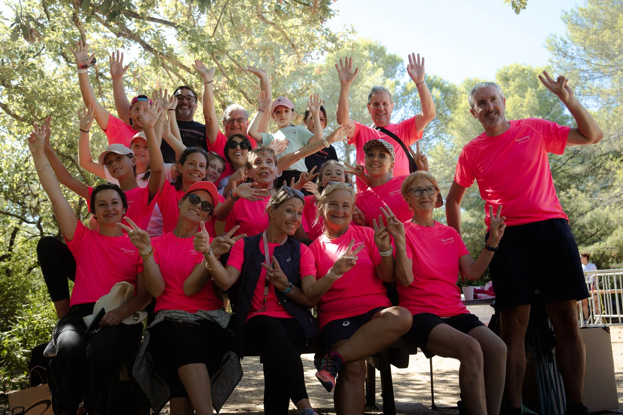 Groupe de personnes souriantes portant des t-shirts roses, posant pour une photo dans un parc en plein air avec des arbres en arrière-plan.