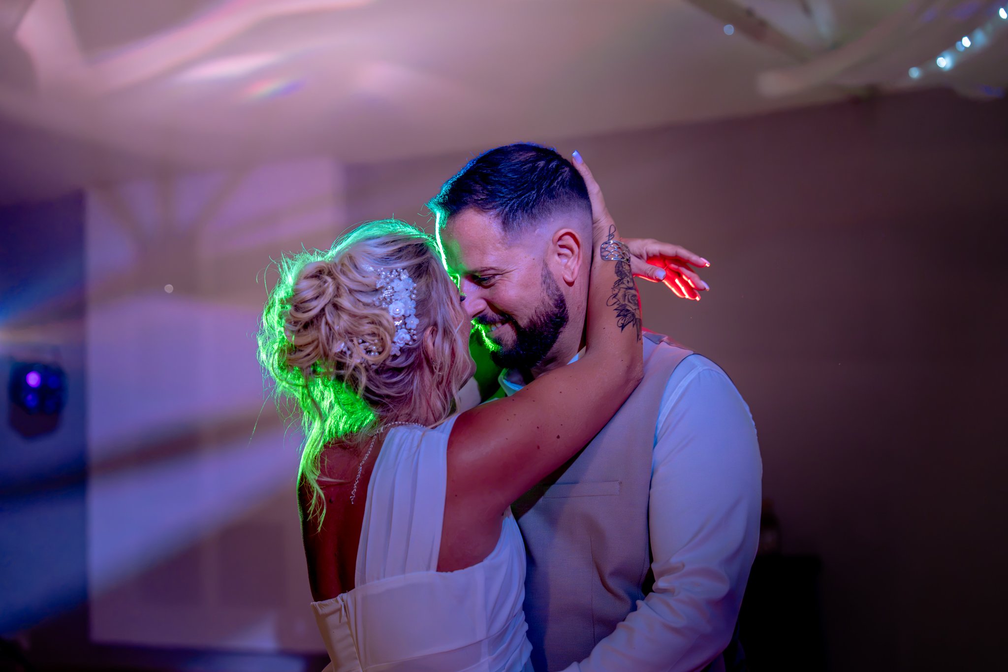 Un couple danse étroitement dans un cadre festif avec éclairage coloré, une ambiance romantique et joyeuse.