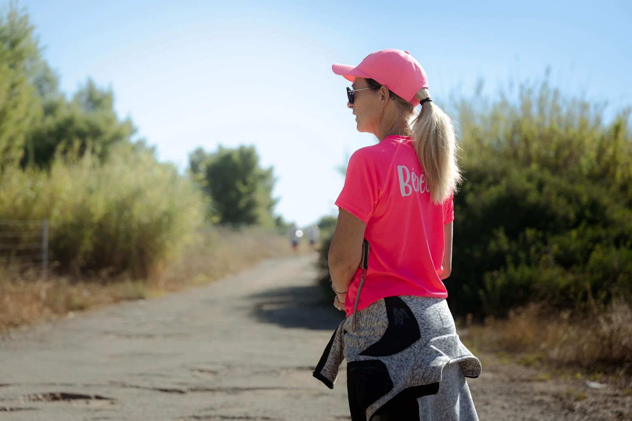 Une femme habillée en rose et gris pratique la marche en plein air sous un ciel ensoleillé.