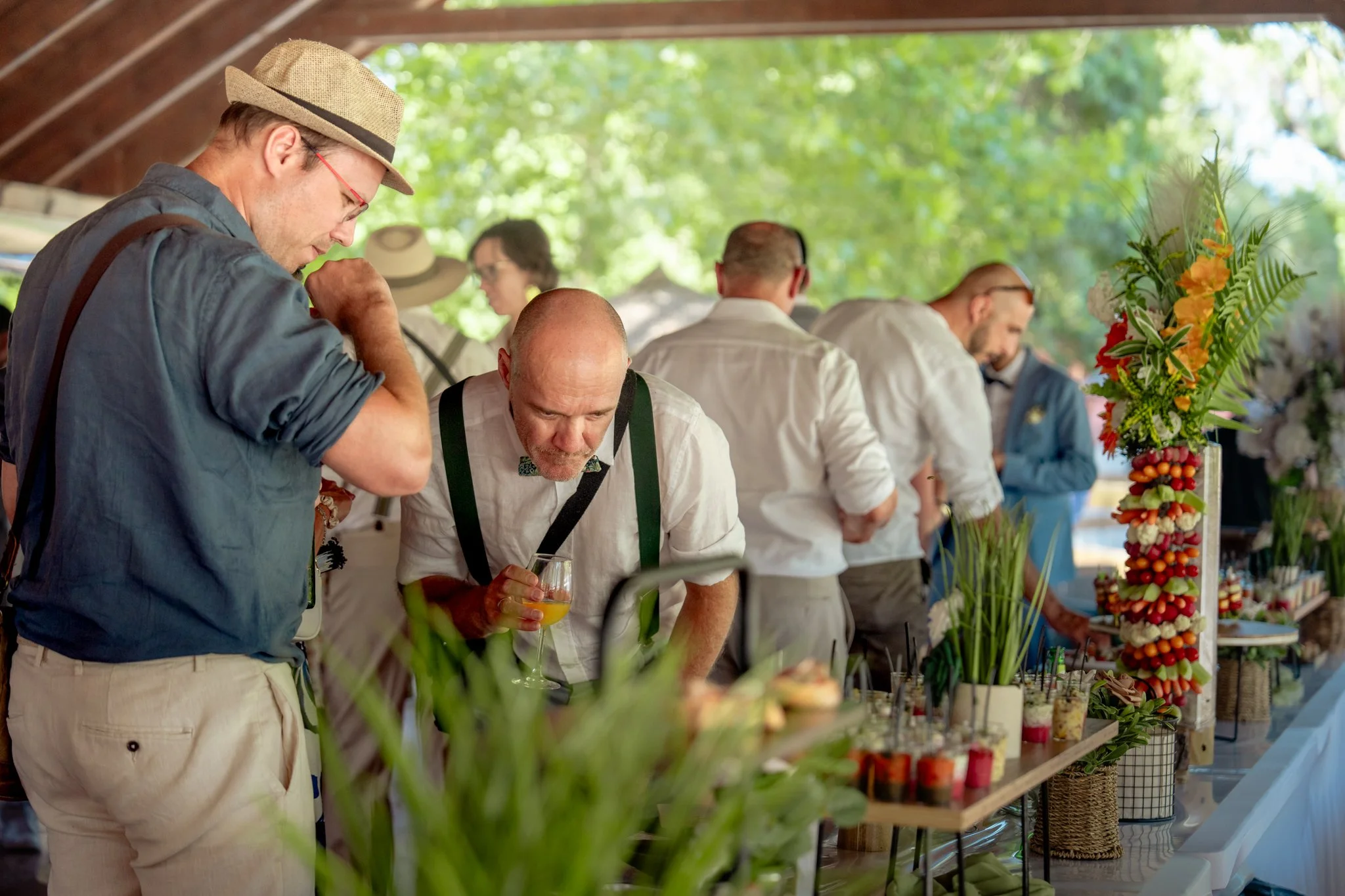 Groupe de personnes dégustant des plats lors d'un événement en plein air, avec un décor naturel et un stand avec des fleurs colorées.