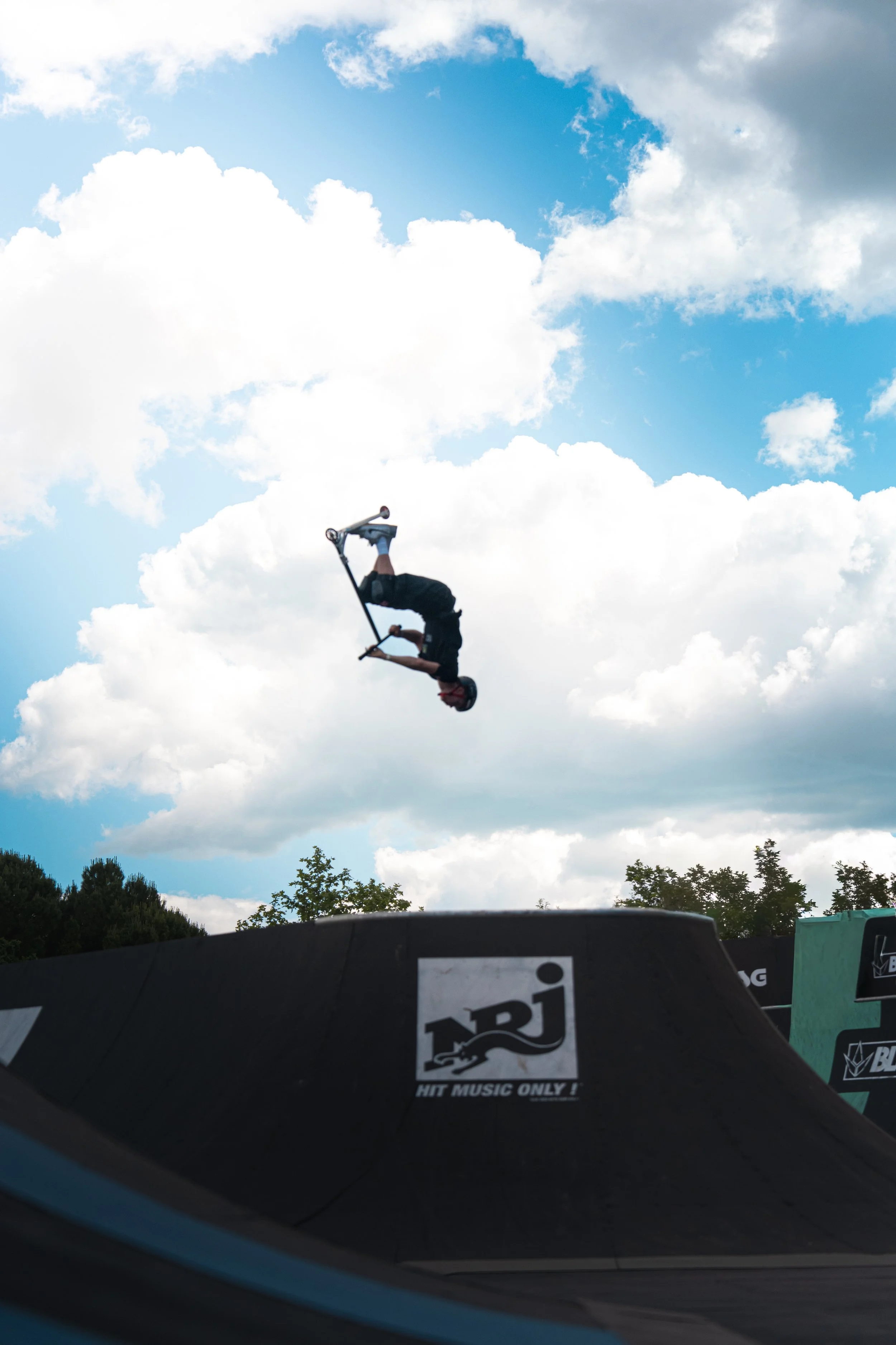 Un skateur effectuant une figure aérienne dans un skatepark avec un ciel nuageux en arrière-plan.