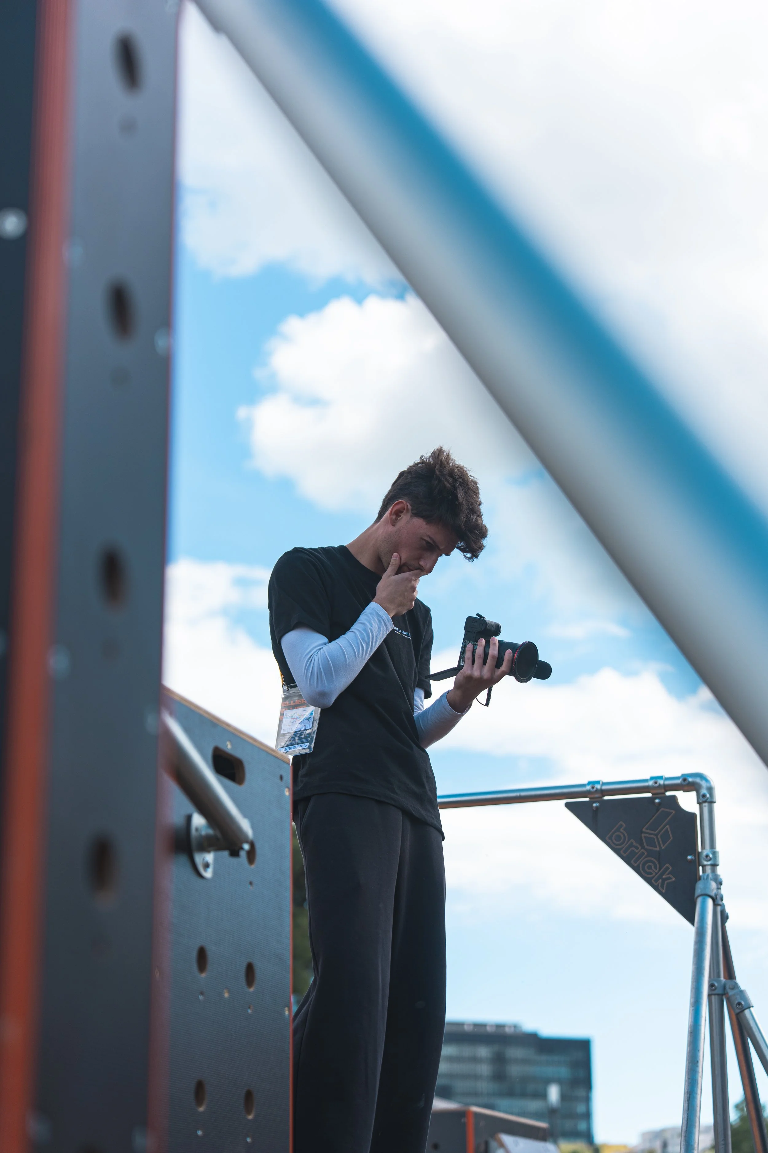 Un jeune homme regarde un smartphone lors d'une activité en extérieur, avec un ciel bleu et des nuages en arrière-plan.