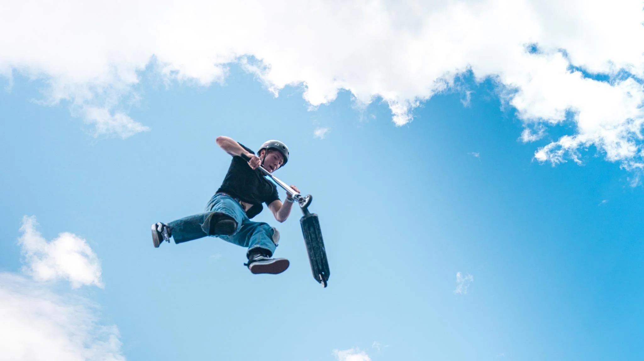 Un jeune homme en casque pratique le scooter des neiges dans un ciel bleu avec des nuages.