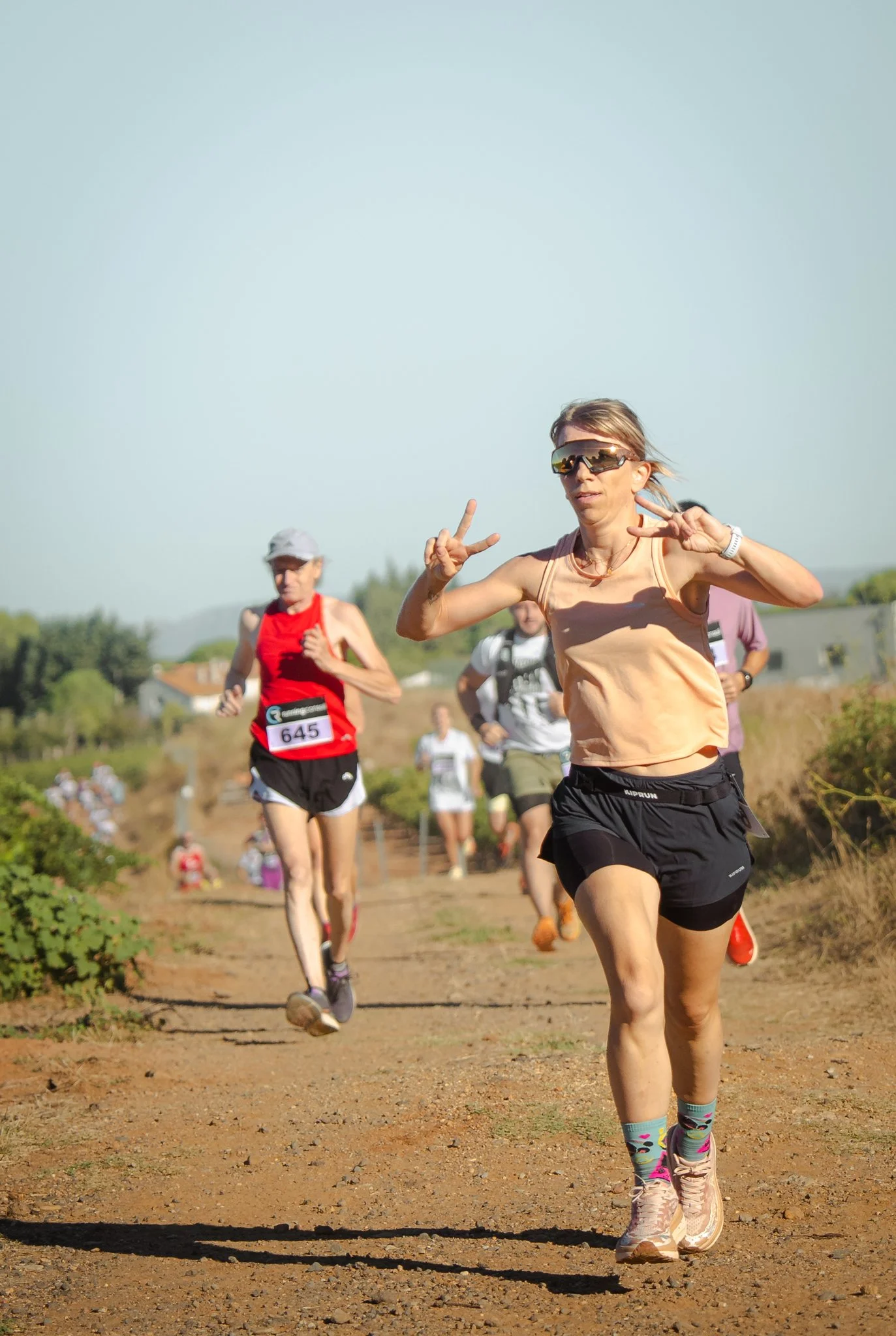Des coureurs participant à une course de trail sur un chemin de terre en plein air, avec des montagnes et des arbres en arrière-plan.