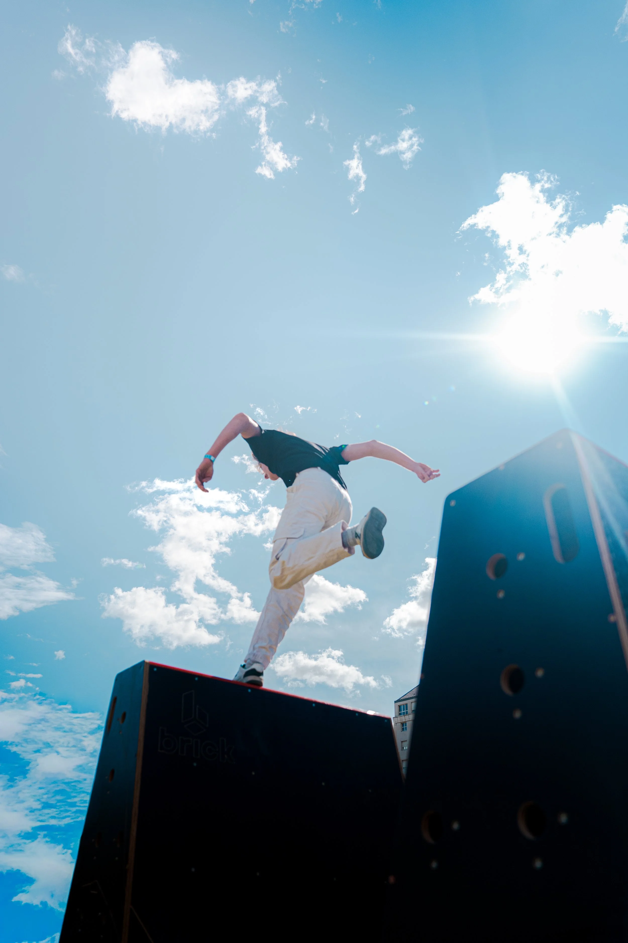 Une personne en train de sauter d'une scène ou d'une plateforme lors d'un spectacle ou d'une performance en extérieur, avec un ciel bleu et des nuages en arrière-plan.