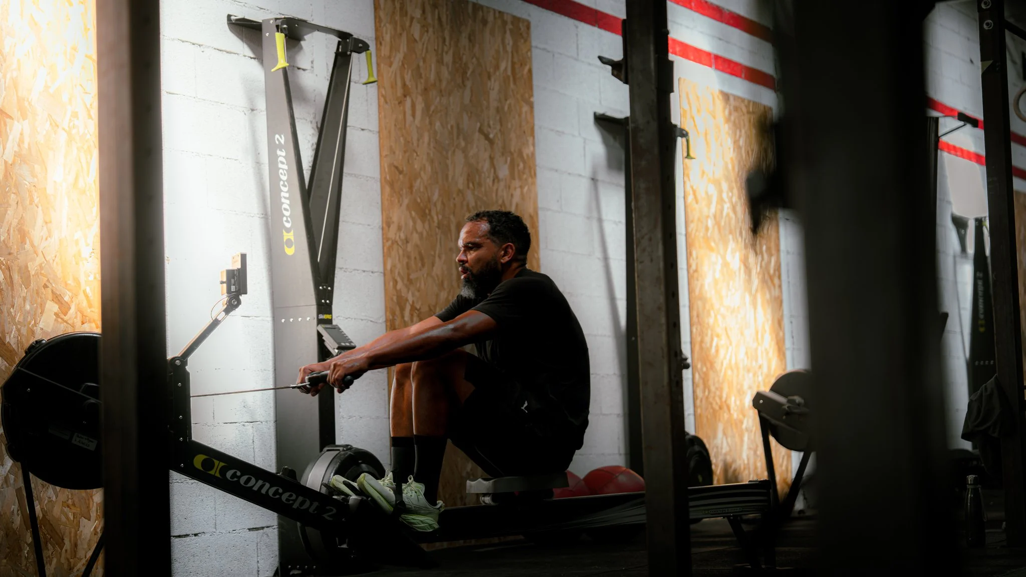 Homme assis sur un banc de musculation dans une salle de sport, en train de faire des exercices avec une machine de rameur.