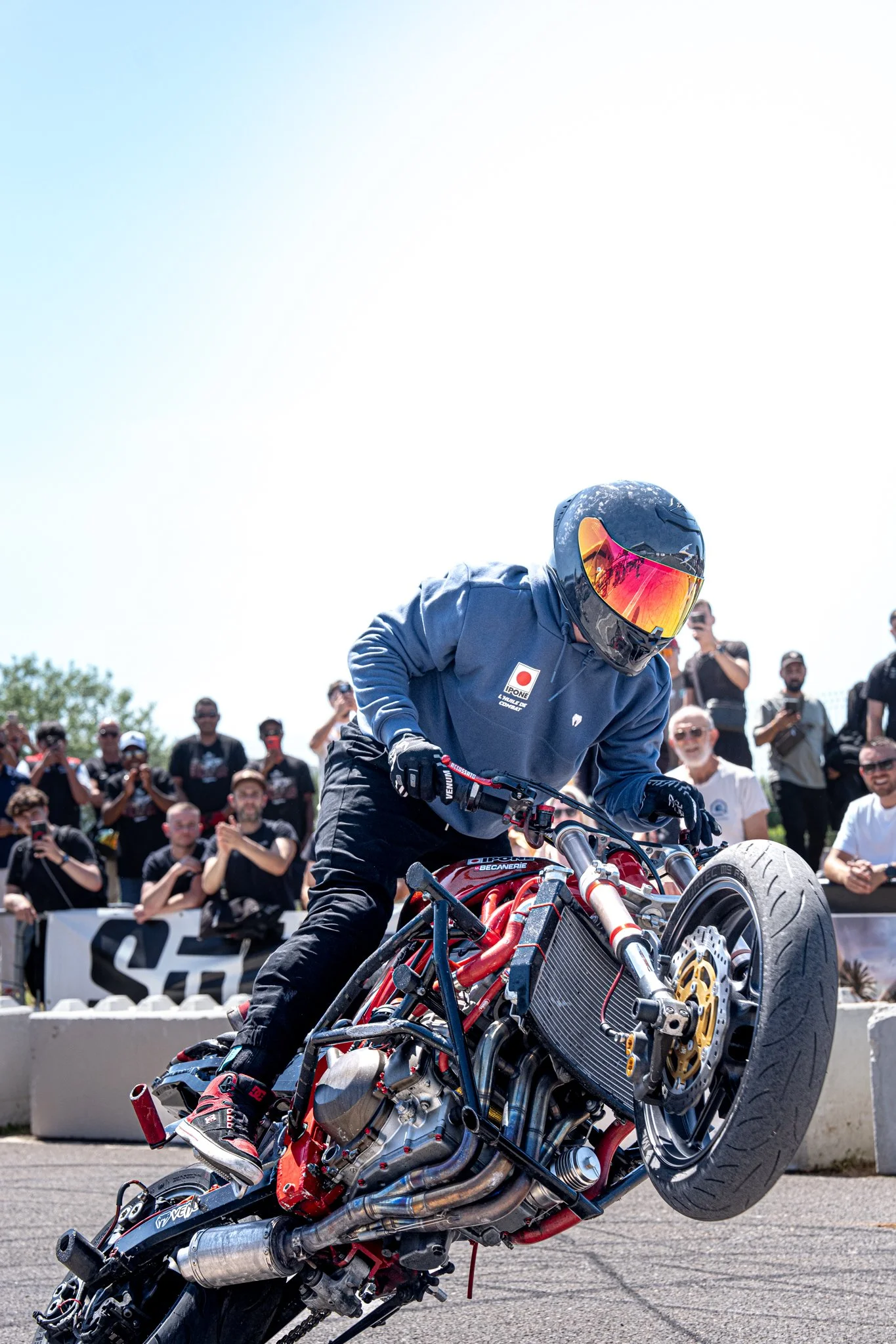 Un homme en casque et vêtements de protection participe à une démonstration de motocross ou stunt avec une moto en équilibre.