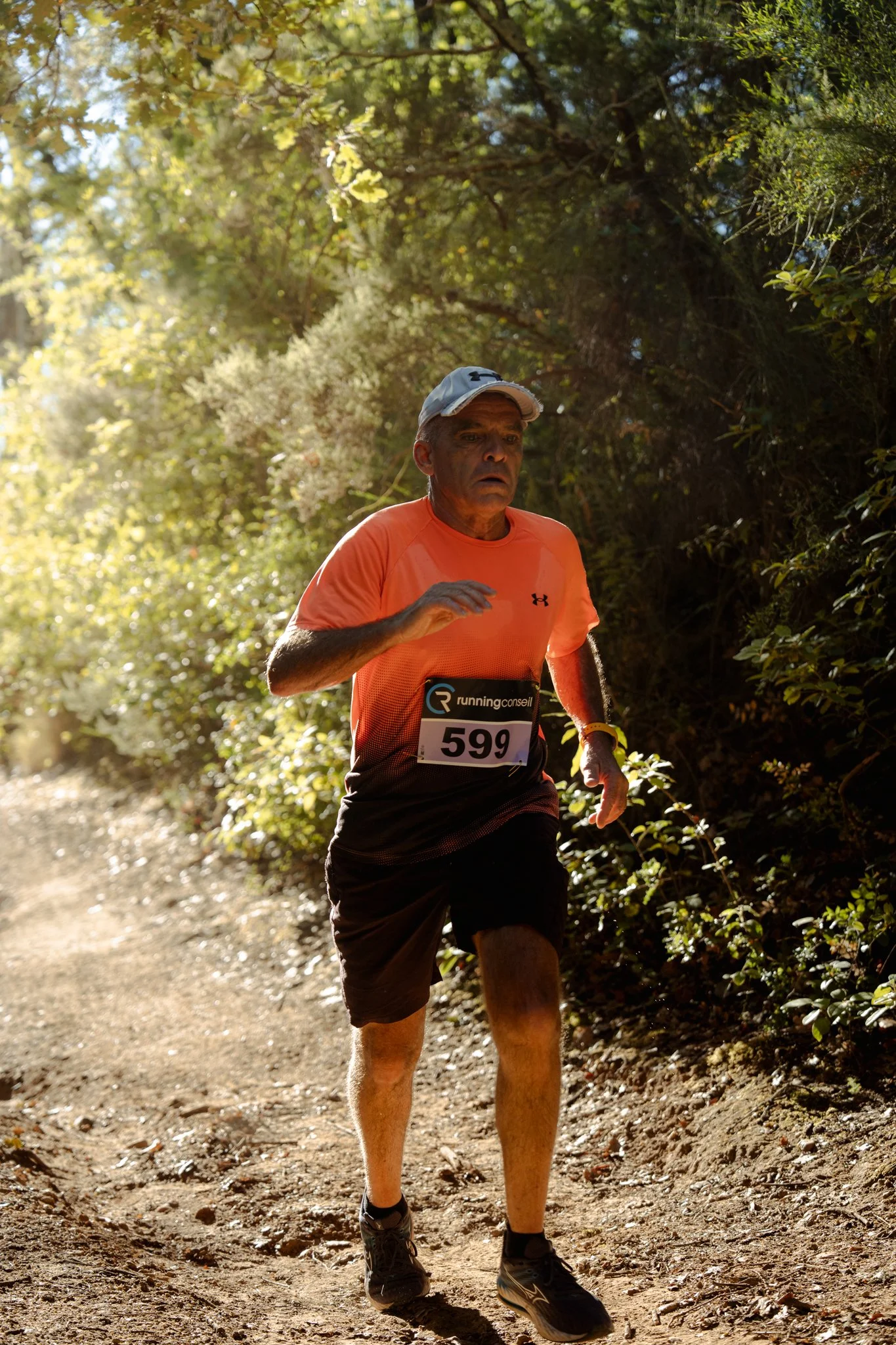 Un homme court dans un sentier bordé d'arbres, portant un t-shirt orange, un chapeau blanc et un numéro de course 599