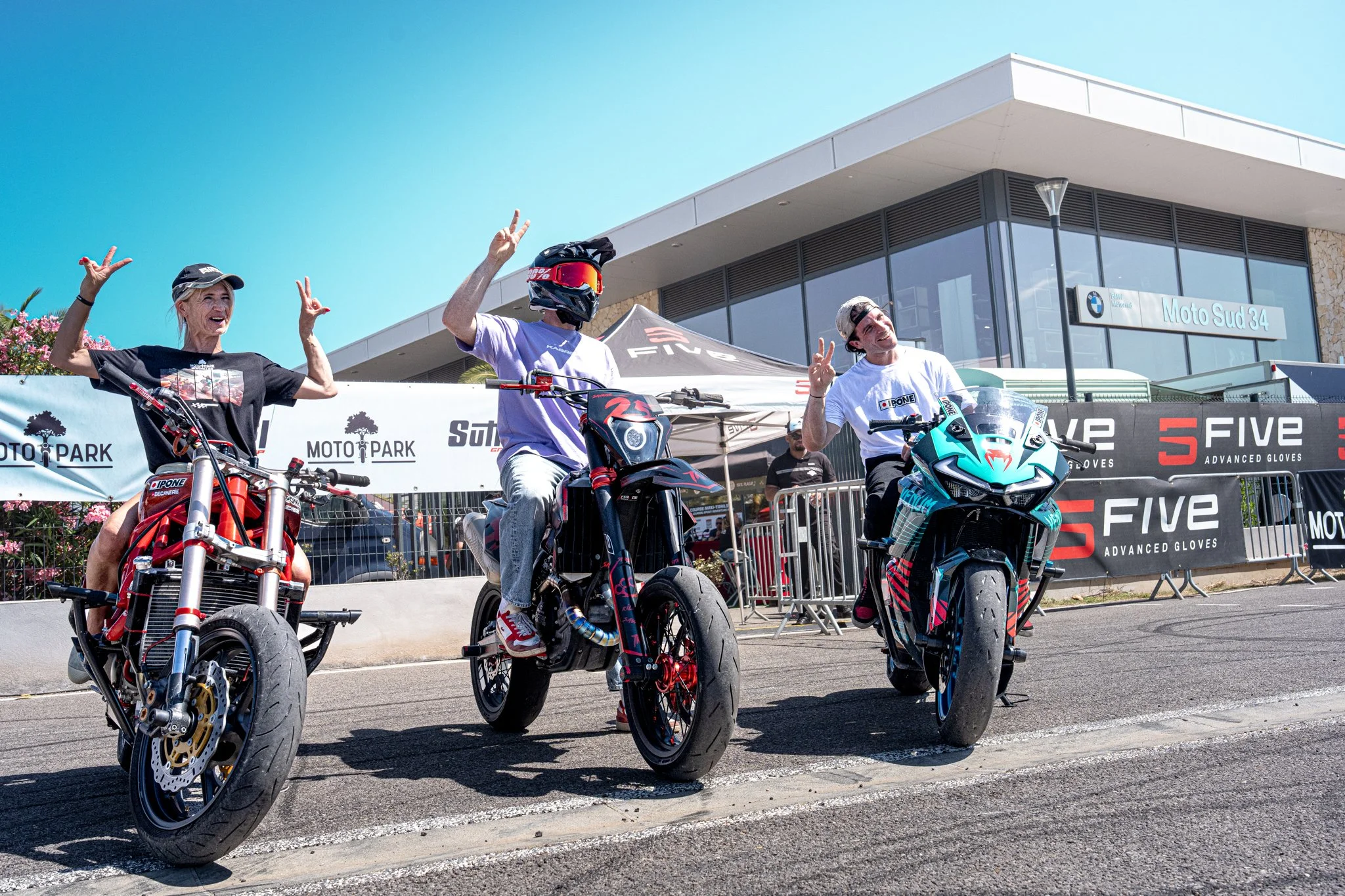 Trois personnes souriantes sur des motos électriques en extérieur devant un bâtiment moderne avec un panneau 'Moto Sud 34', sous un ciel bleu.