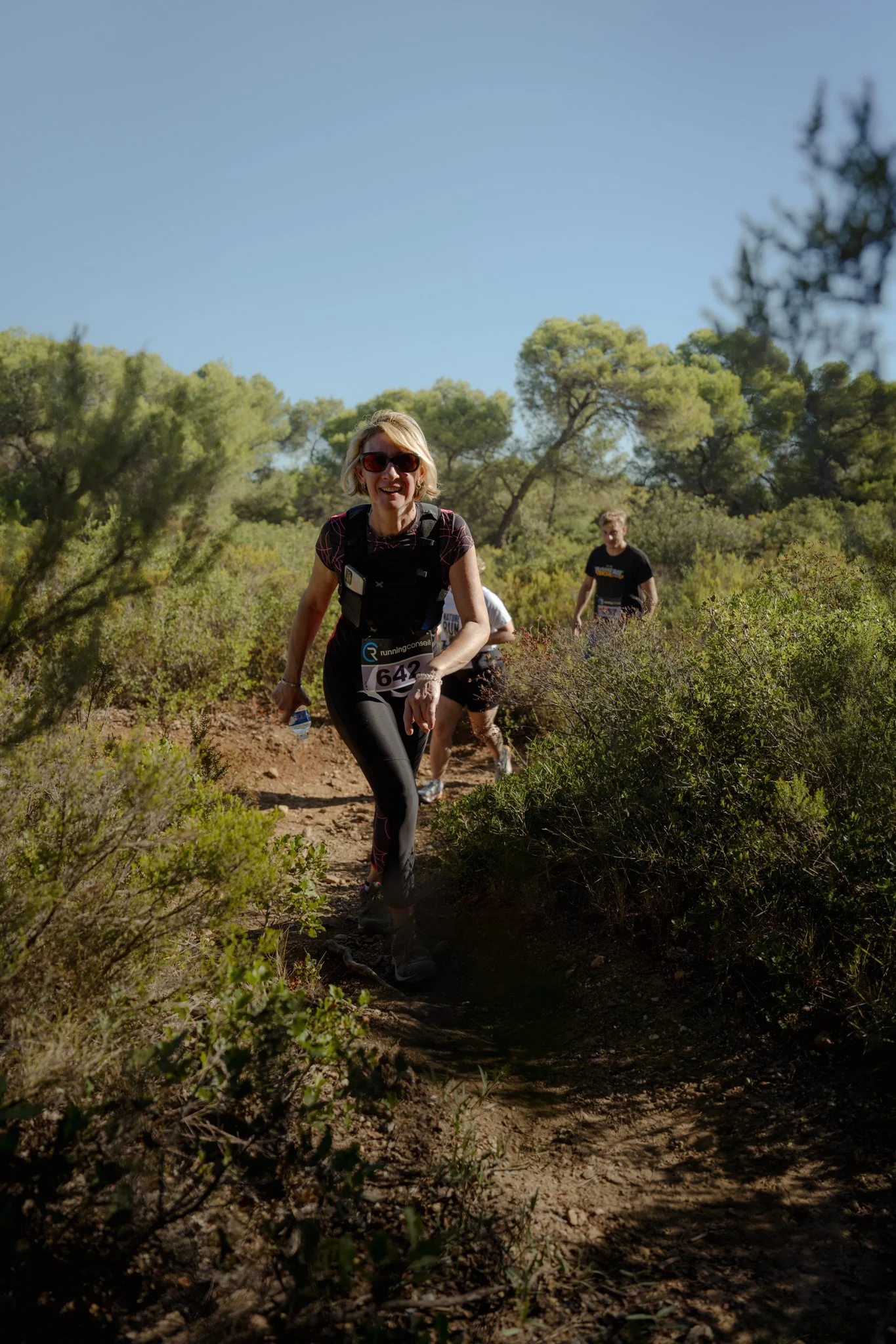 Femmes courant sur un sentier en pleine nature avec des arbres et un ciel bleu clair.