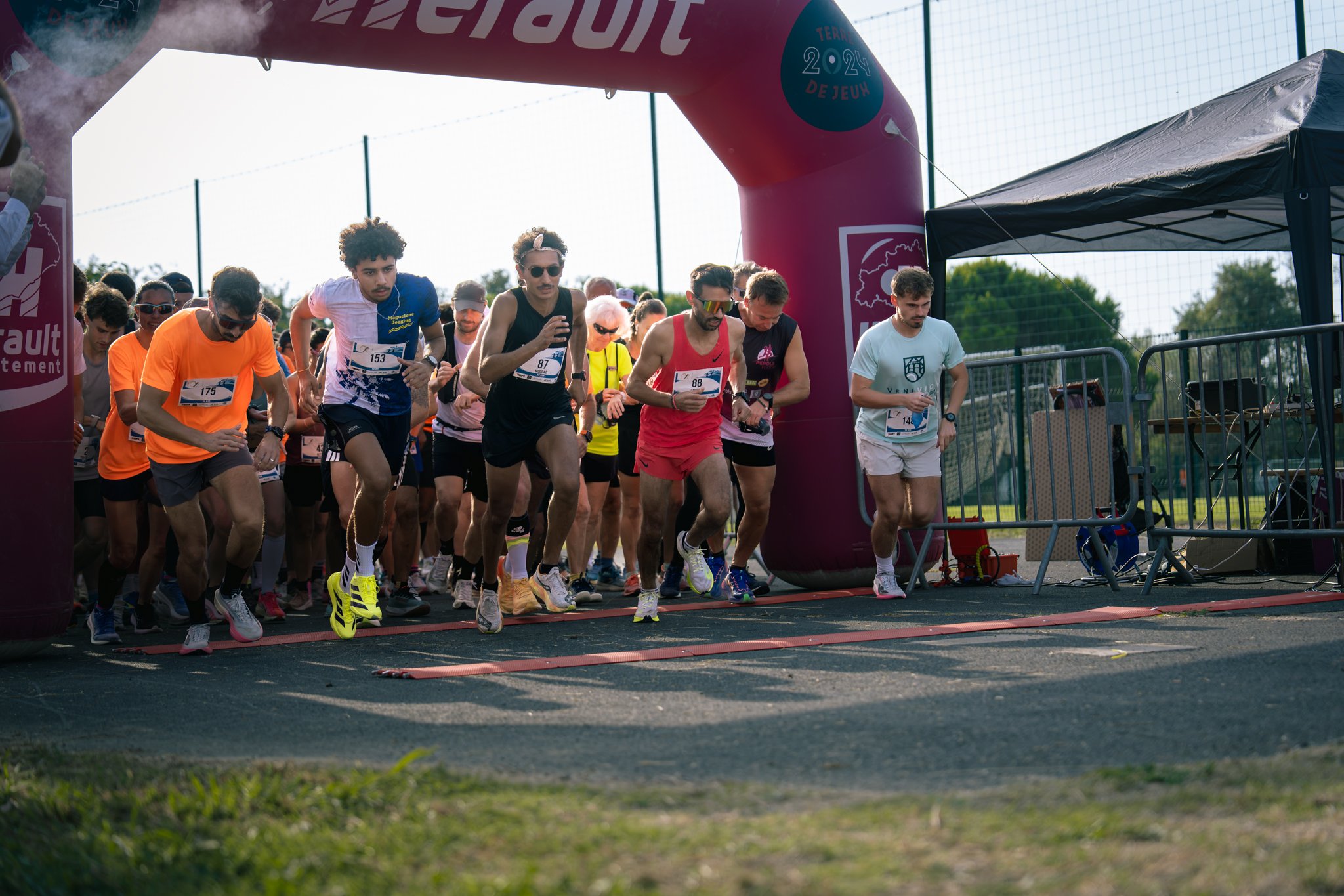 Groupe de coureurs lançant un départ lors d'une course sur piste, sous un arc de départ rose.