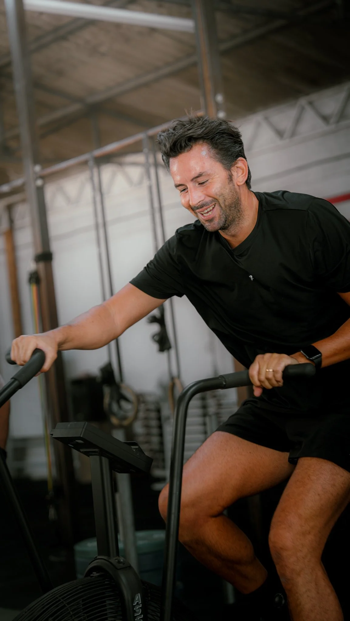 Un homme souriant faisant du vélo d'appartement dans une salle de sport.
