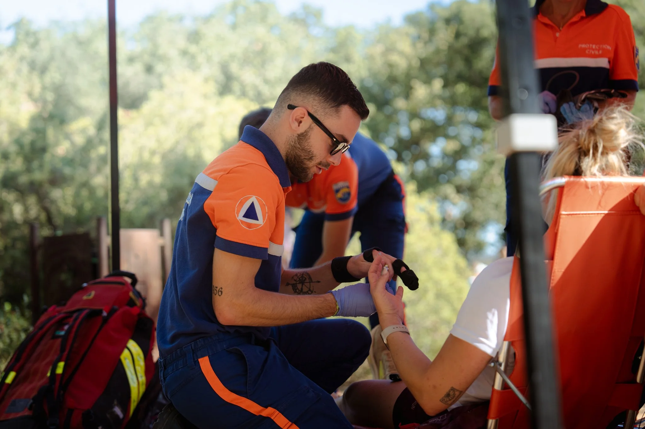 Une équipe de secouristes en uniforme orange aidant une personne lors d'une opération dans un environnement extérieur. Les secouristes semblent en train de prêter attention à une situation d'urgence.