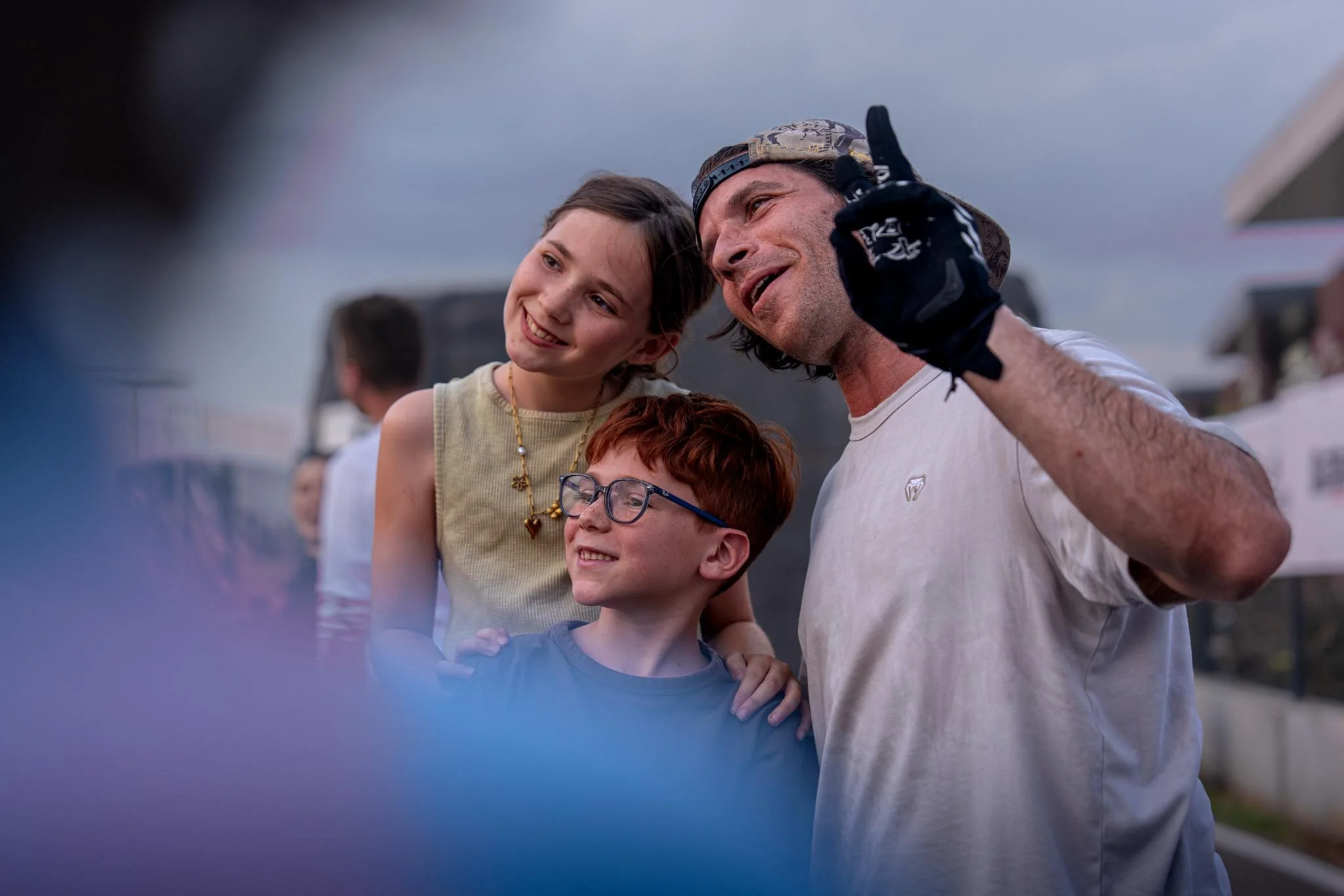 A group of people, including two children and an adult, smiling and enjoying an outdoor event under cloudy skies.