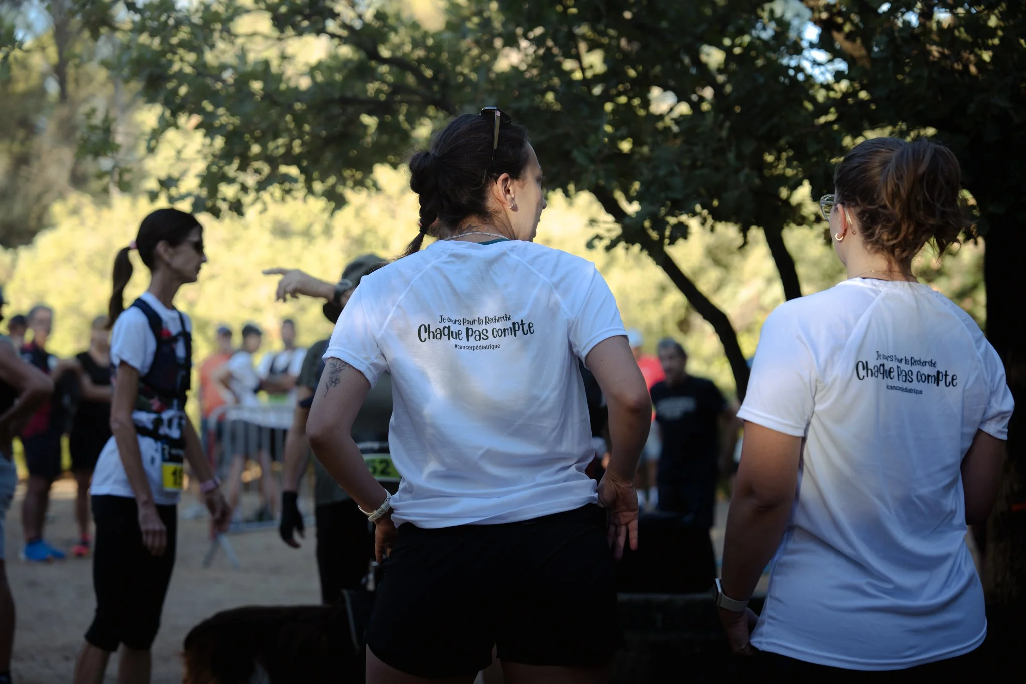 Groupes de personnes en vêtements de course participant à un événement de course dans un parc, portant des t-shirts avec le message 'Je cours pour la recherche, Chacun pas compte'.