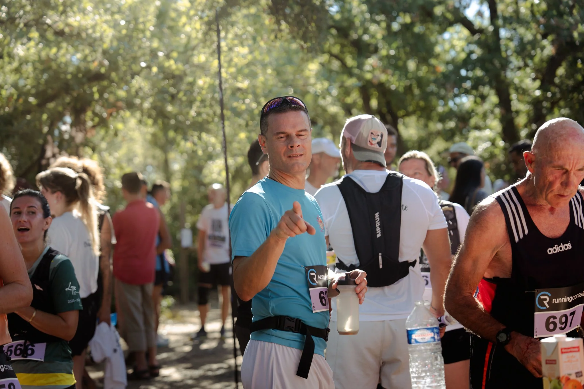 Groupe de coureurs participant à une course dans un parc en plein air, certains portant des dossards et des bouteilles d'eau.