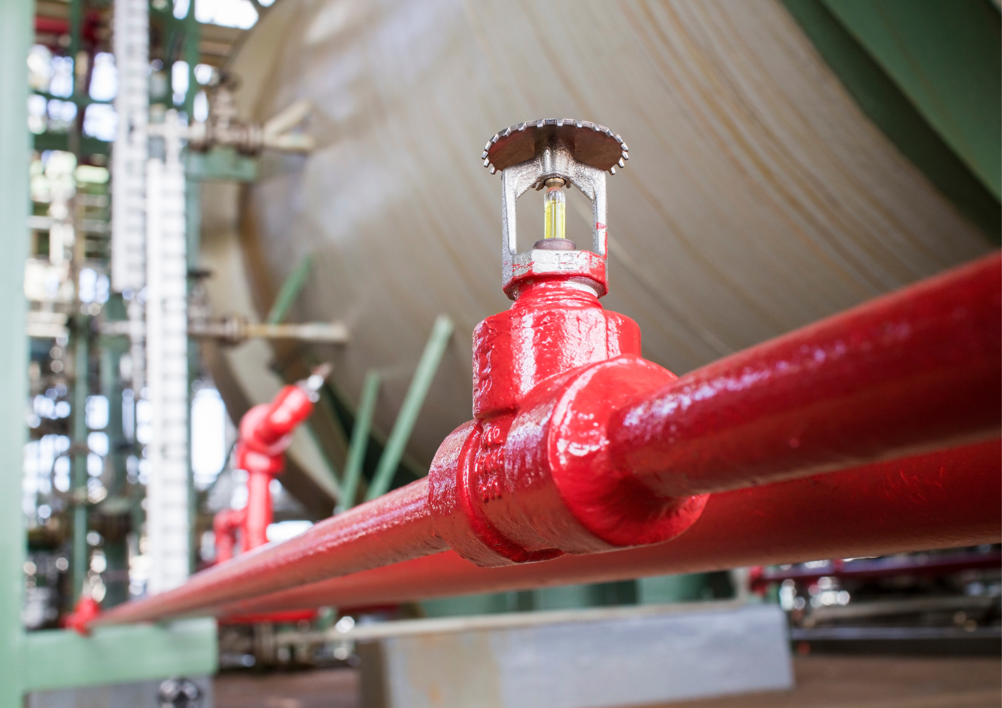 Close-up of a red fire hose valve with a yellow pressure gauge, mounted on a red pipe, in an industrial or warehouse setting.