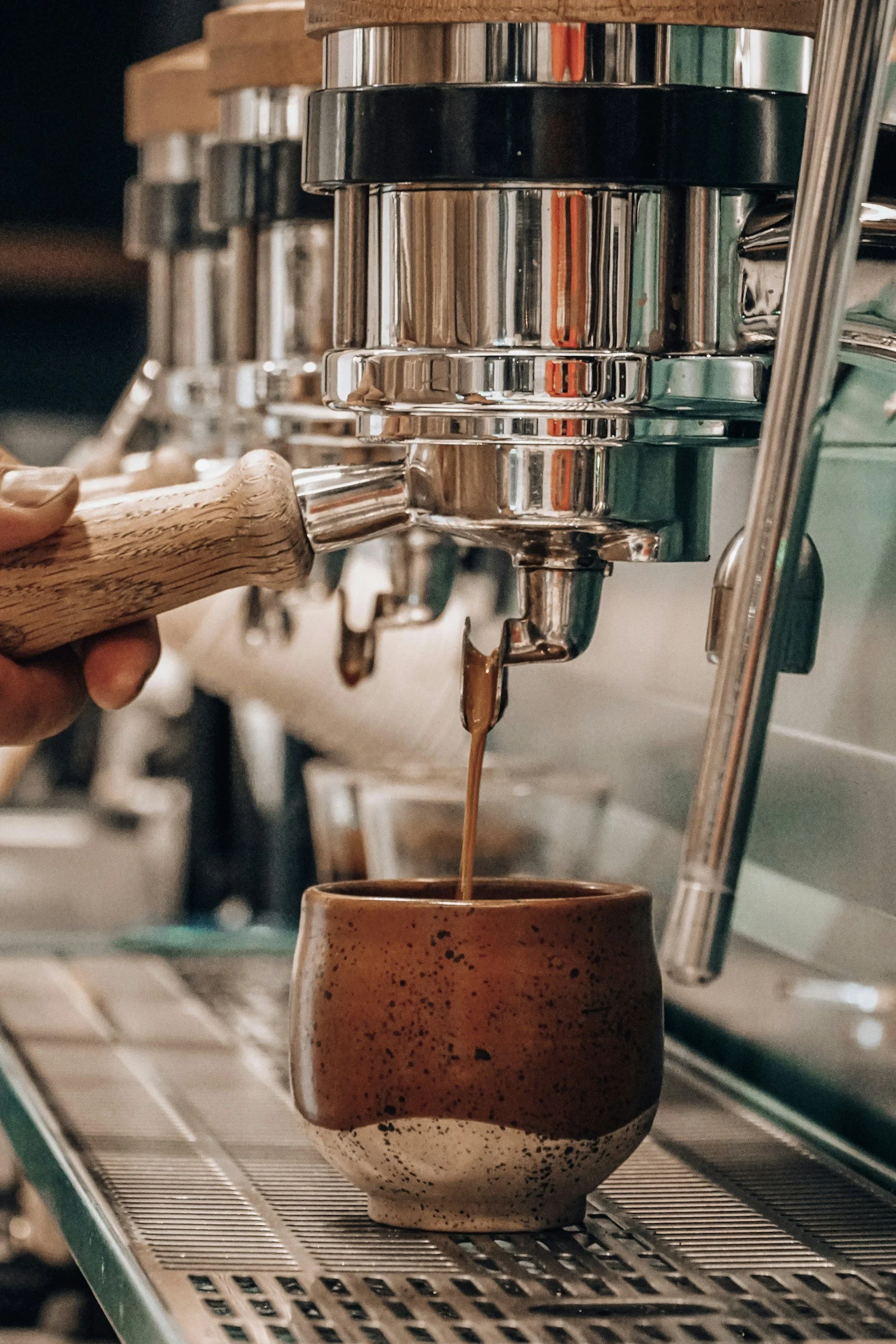Kaffeetropfen fließen aus einer Espressomaschine in eine handgefertigte Keramik tasse.