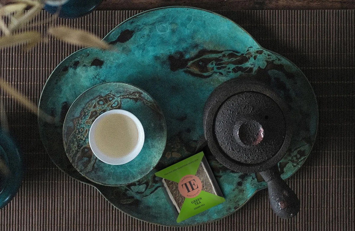 Teekanne, Teetasse mit grünem Tee, Teebeutel mit grüner Verpackung auf einer dekorativen Schale.