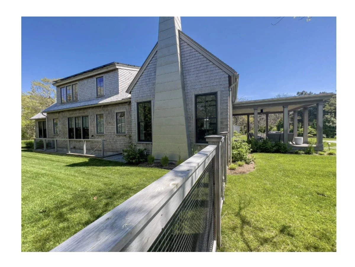 Front view of a modern house with a garden, wooden fence, and a covered patio, under a clear blue sky.