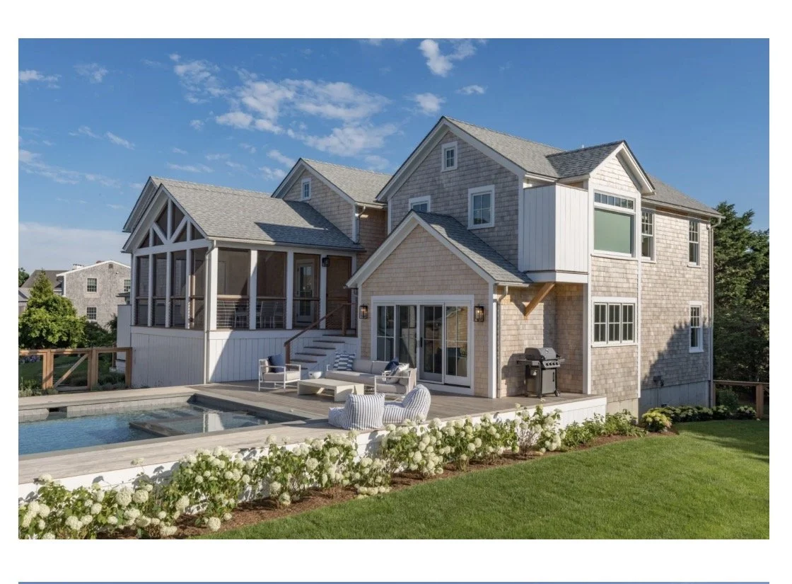 A two-story house with a backyard featuring a swimming pool, outdoor seating, a barbecue grill, and landscaped garden with white flowers.