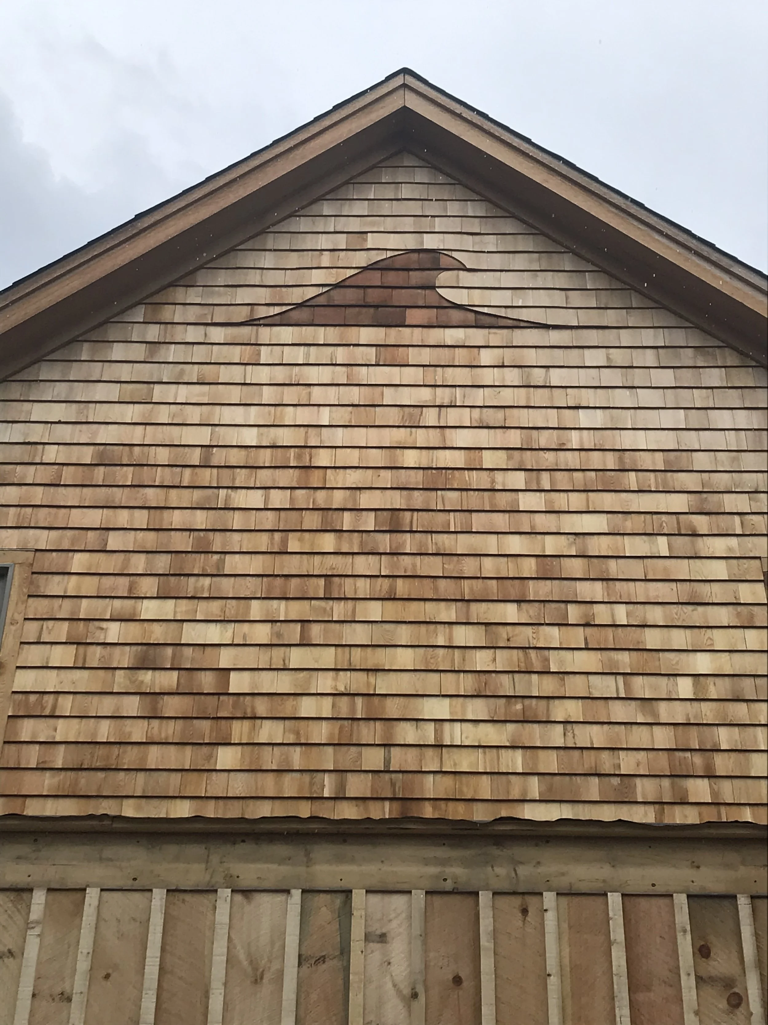 Close-up of a house's front exterior showing wooden shingles and part of the framing at the bottom, with an incomplete section of the wall.