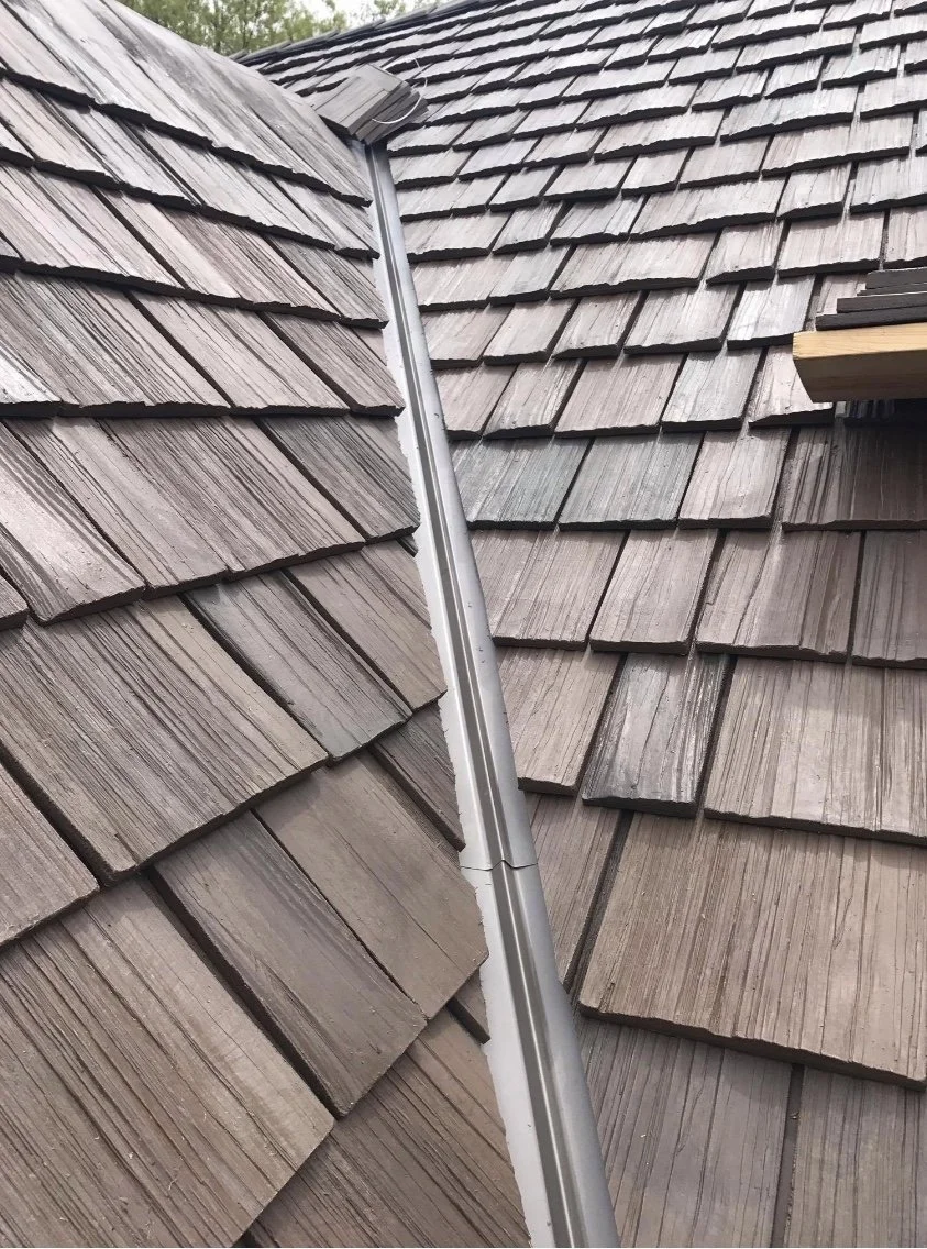 Close-up of a roof with brown wooden shingles and a metal ridge cap.