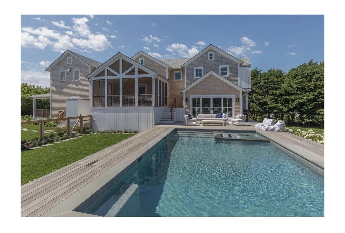 A modern house with a pool on a sunny day, featuring an outdoor lounge area with white furniture, and surrounded by greenery.