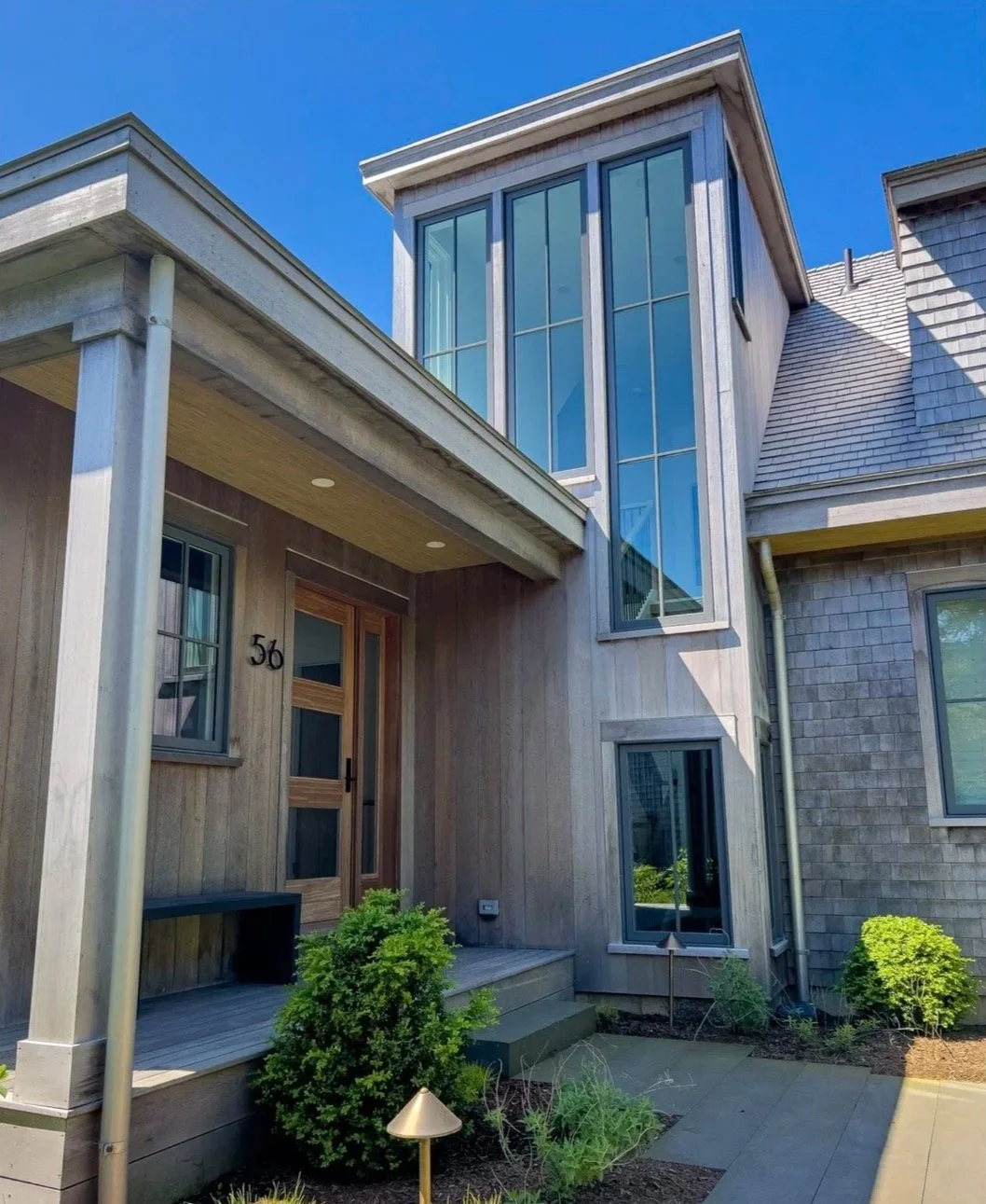 Modern house with wooden and shingle exterior, large glass windows, and small landscaped garden in the front yard.
