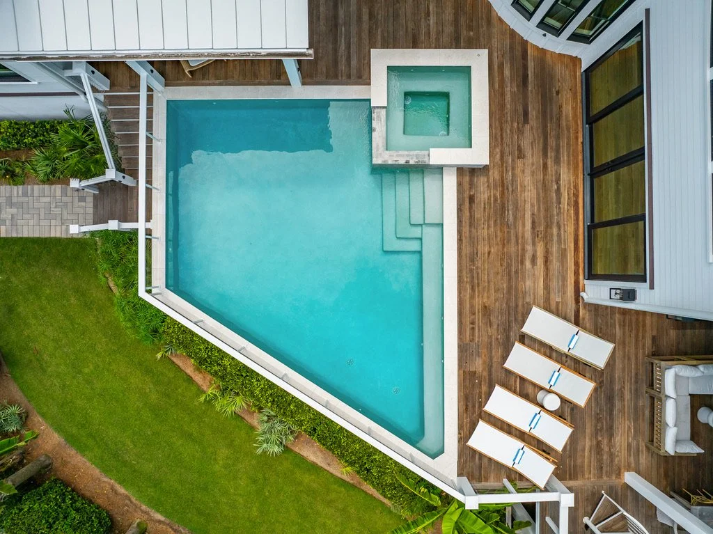 Aerial view of a backyard with a swimming pool, a hot tub, and a wooden deck with lounge chairs and a seating area.