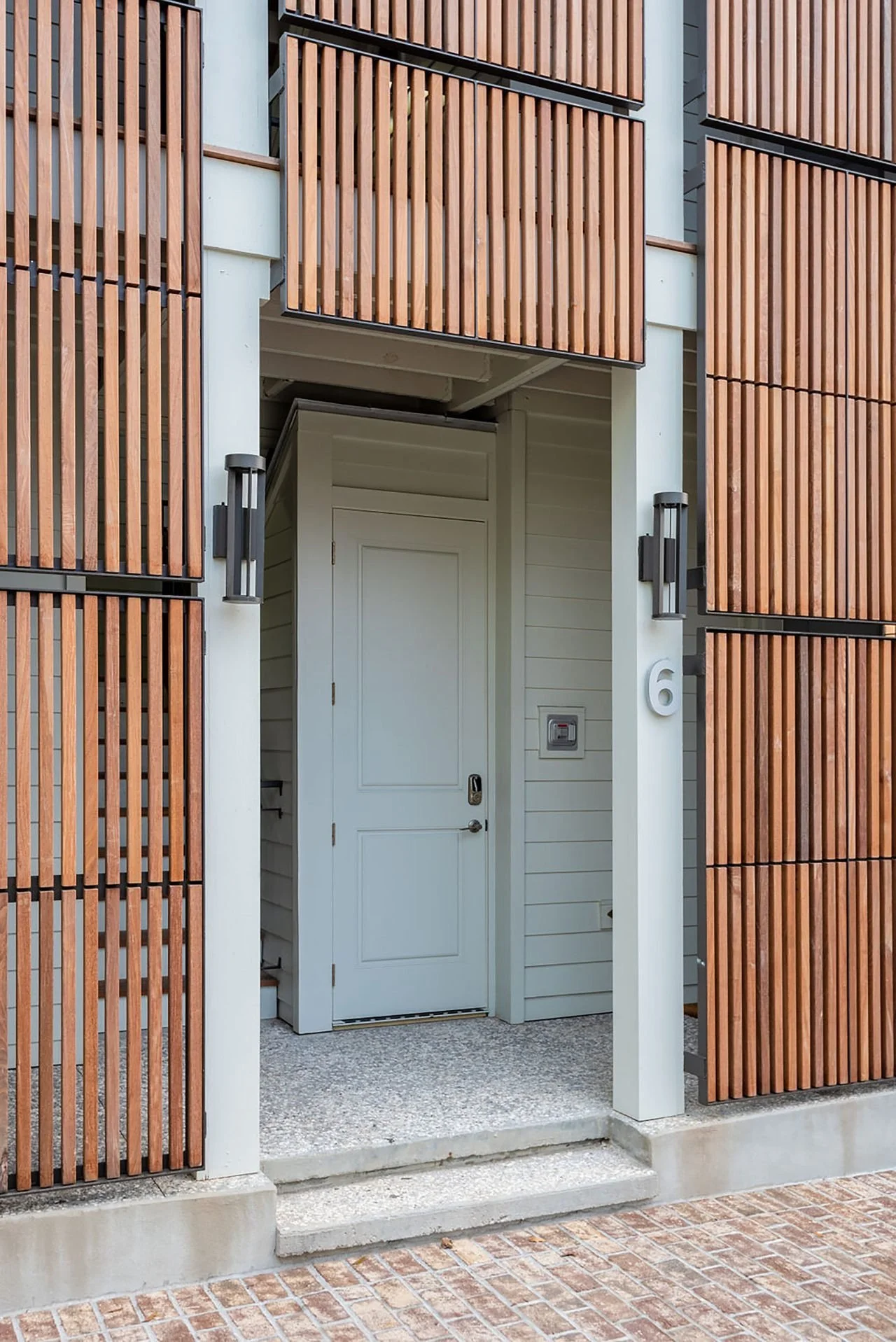 Modern building entrance with white door, wooden slatted panels, and wall-mounted lights.