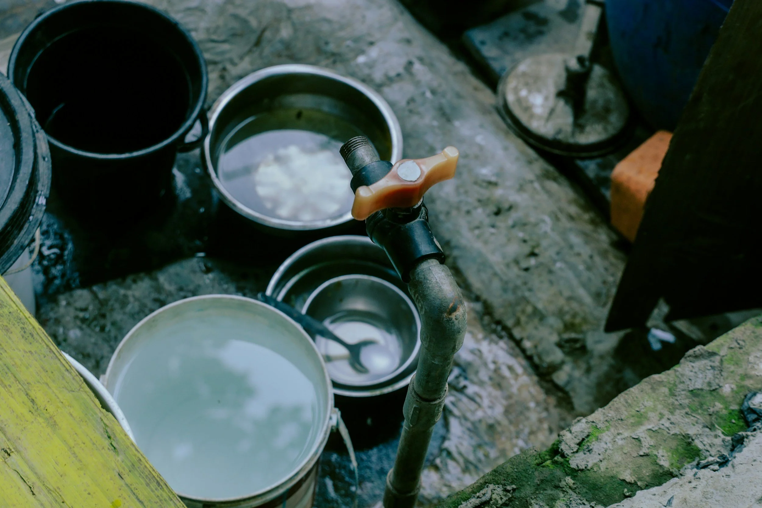 A plumbing setup with a pipe connected to a water source, two buckets containing water, and concrete flooring. There are also various tools and construction materials around.