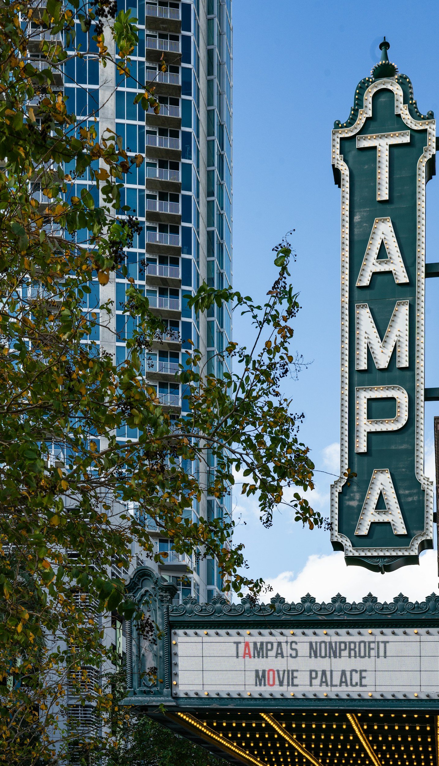 The Avalon Theater marquee sign with the message about AmpA's nonprofit Move Palace, showing a tall modern blue glass building and trees in an urban setting.