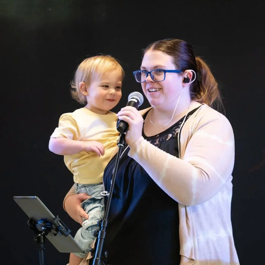 Woman holding a child and singing into a microphone.