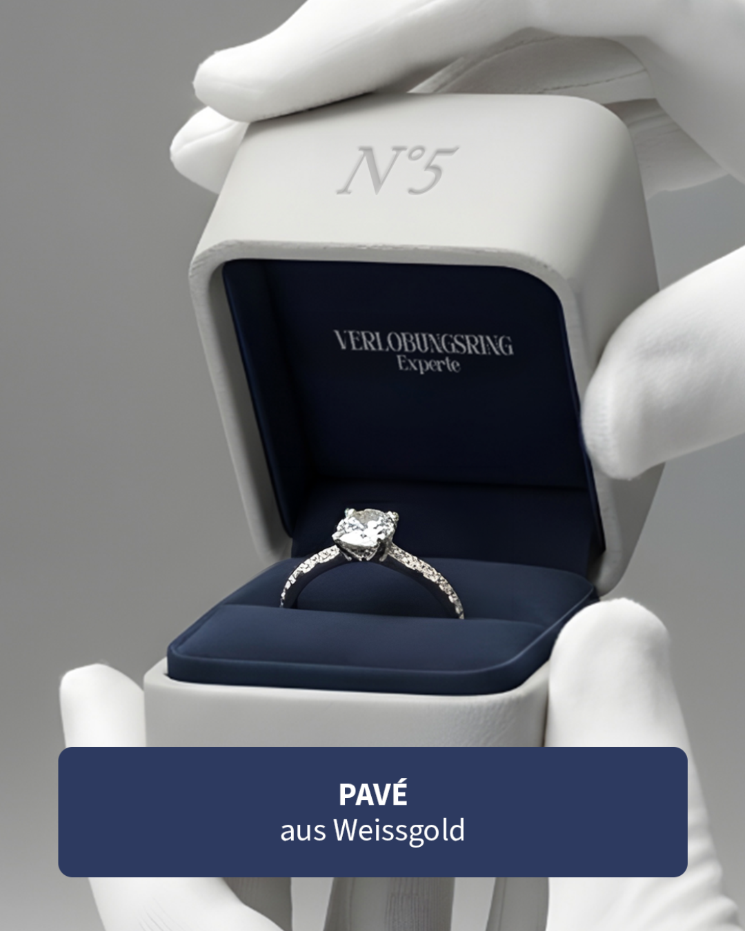 Ein Verlobungsring mit Diamanten in einer schwarzen Schmuckschatulle, gehalten von weißen Handschuhen, mit der Aufschrift 'VERLOBUNGSRING Experte' im Inneren der Schachtel.