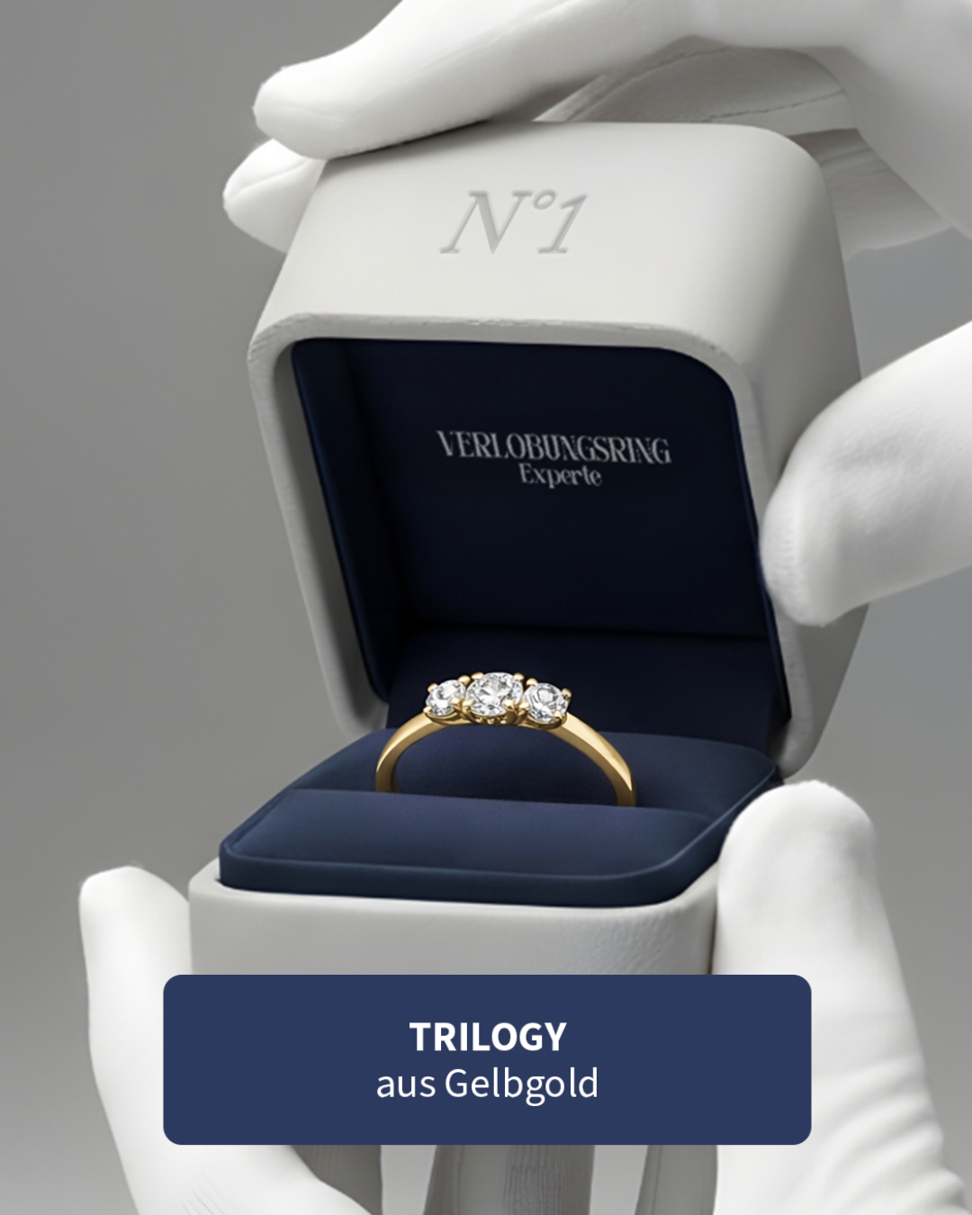 Ein goldener Ring mit drei Diamanten in einer schwarzen Schmuckschatulle, gehalten von weißen Handschuhen.