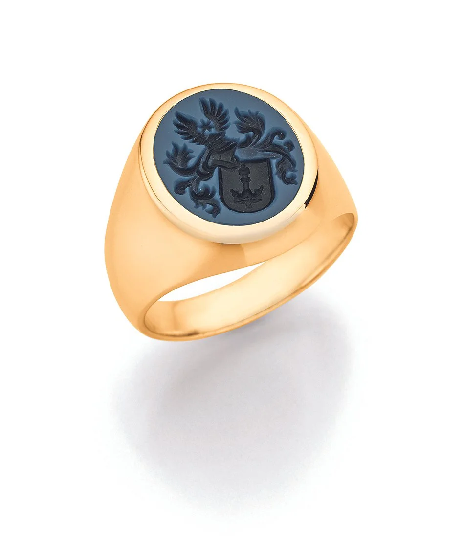 Nahaufnahme eines goldenen Siegelrings mit einem blauen Wappen, das einen Adler und ein Boot zeigt.