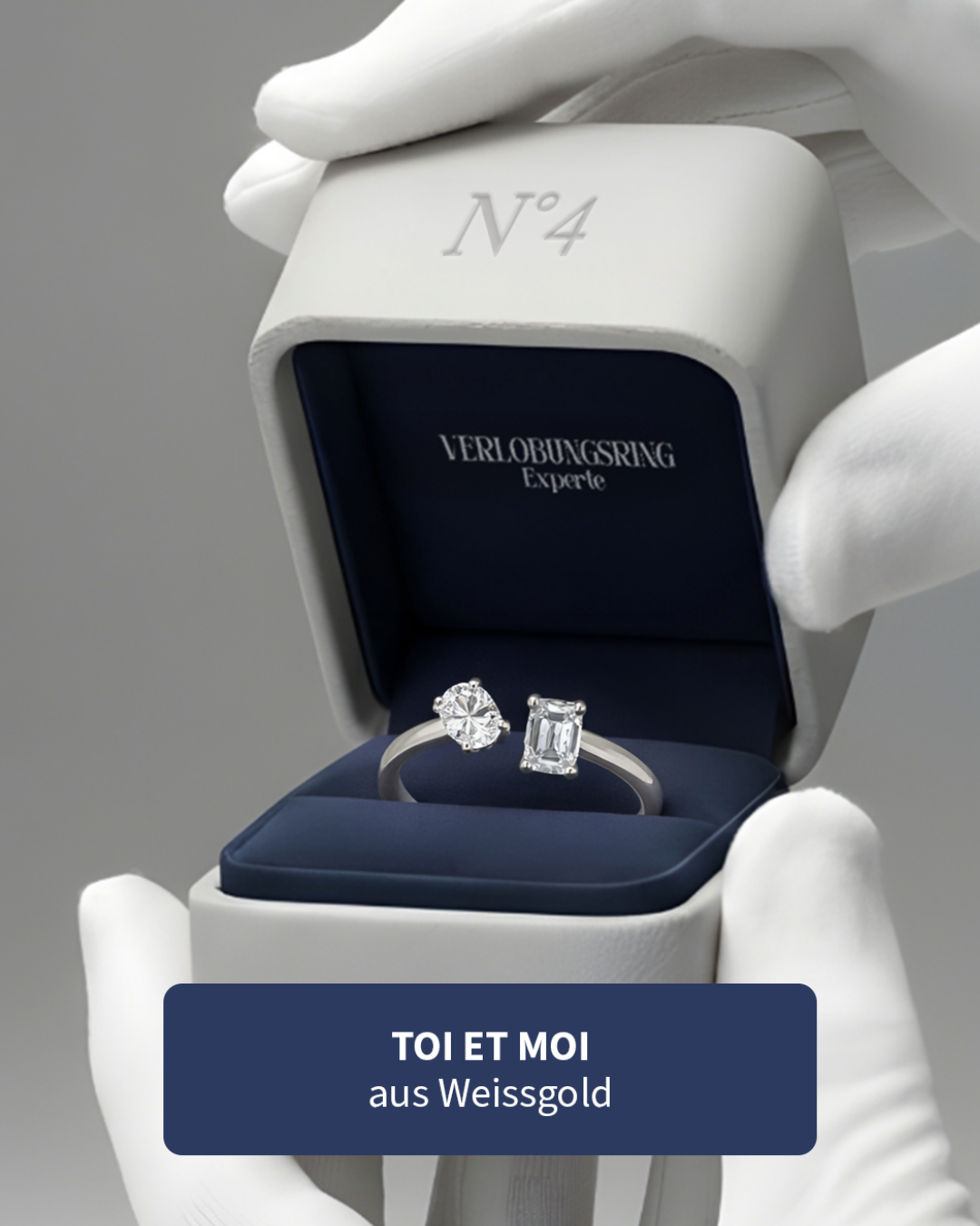 Ein offener Ringkasten mit einem Diamantring aus Weißgold, mit der Beschriftung TOI ET MOI und VERLOBUNGSRING auf schwarzem Hintergrund.