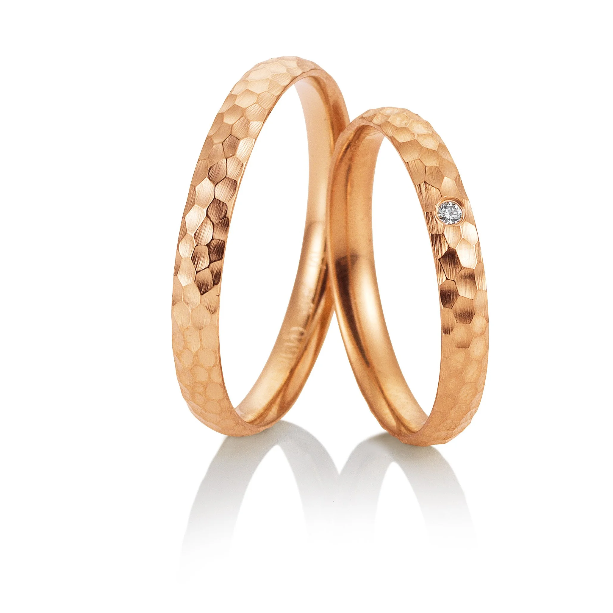 Zwei goldene Ringe mit einer gewellten Oberfläche, einer davon mit einem kleinen Diamanten, auf weißem Hintergrund.