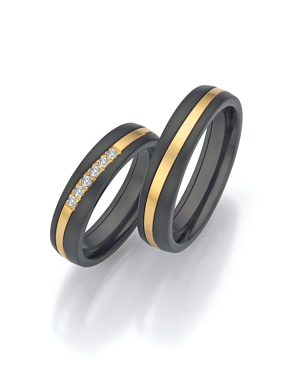 Zwei schwarze Eheringe mit goldenen Linien, einer davon mit Diamanten, auf weißem Hintergrund.