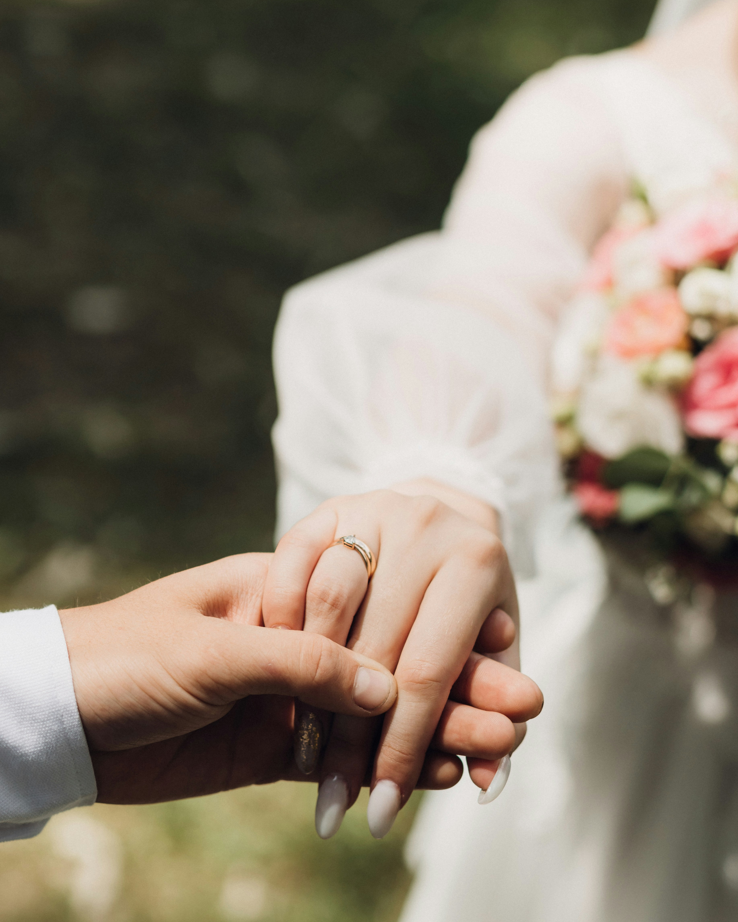 Nahaufnahme wie der Ehemann auf seiner Hochzeit die Hand seiner Braut nimmt, Fokus auf die Hände und den Ehering.