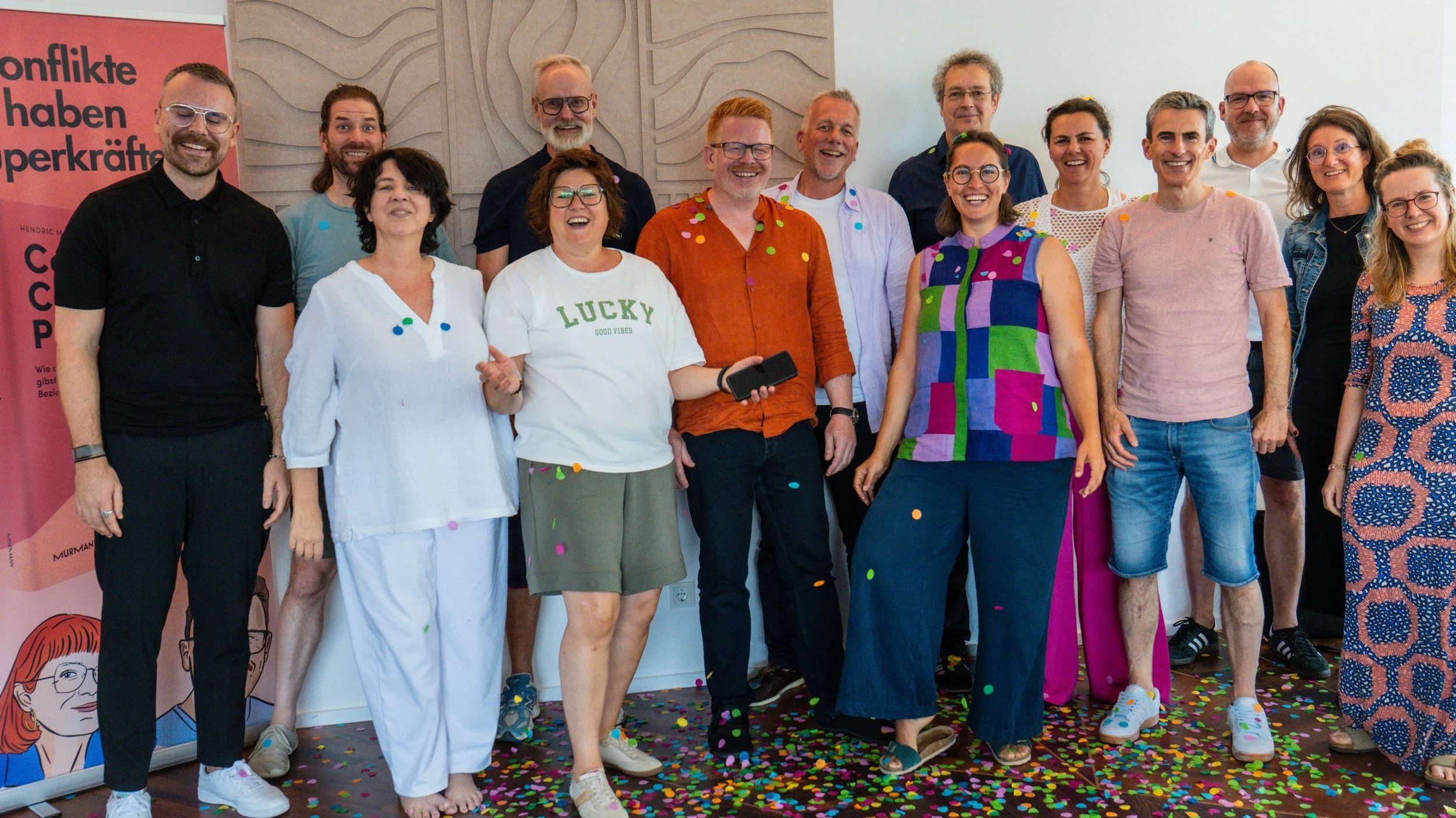 Eine Gruppe lachender Menschen bei einer Feier, mit bunten Konfetti auf dem Boden, die Freude und Geselligkeit zeigt.