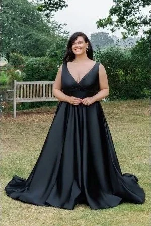 A woman in a long black dress standing on grass in a park with trees and a wooden bench in the background.