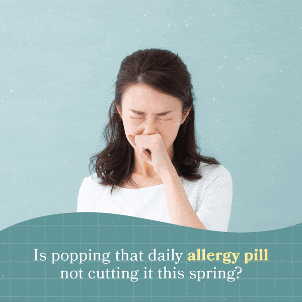 A woman with dark hair, wearing a white top, is sneezing into her fist against a light blue background with water droplets. Text at the bottom asks, "Is popping that daily allergy pill not cutting it this spring?"