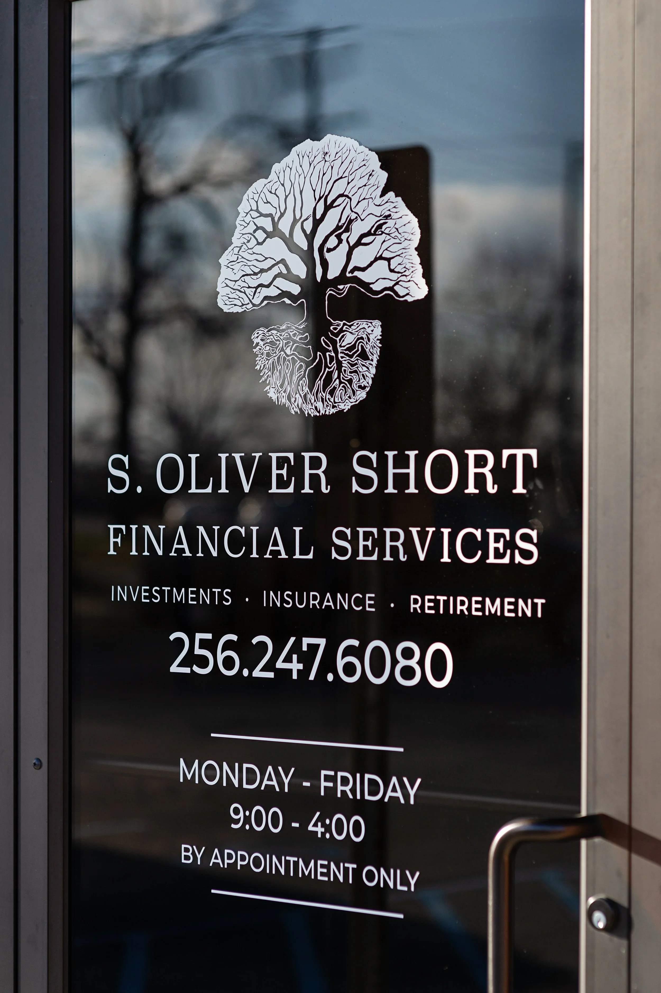 Glass door with logo of a tree and business name 'S. Oliver Short Financial Services' with phone number and business hours displayed.