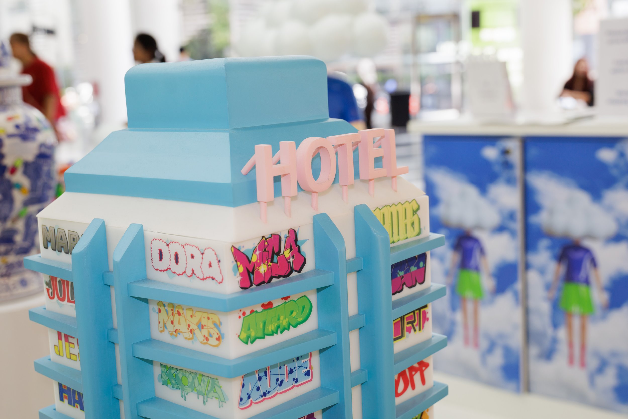 A display of colorful comic book-themed stickers in a retail store, with a blurred background of people shopping and a large window showing outside scenery.