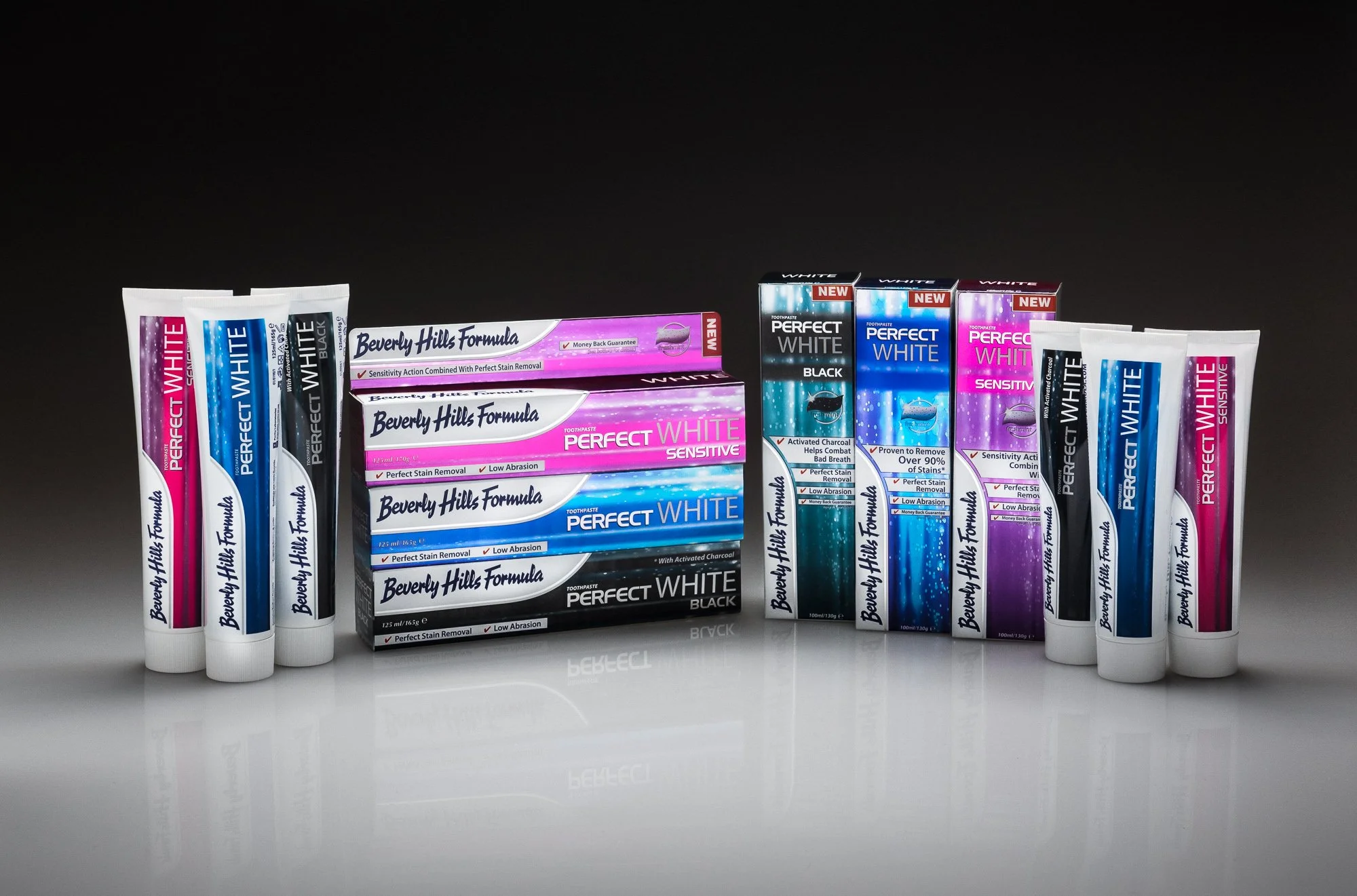 Several tubes of Beverly Hills Formula Perfect White toothpaste and their boxes arranged on a reflective surface against a black background.