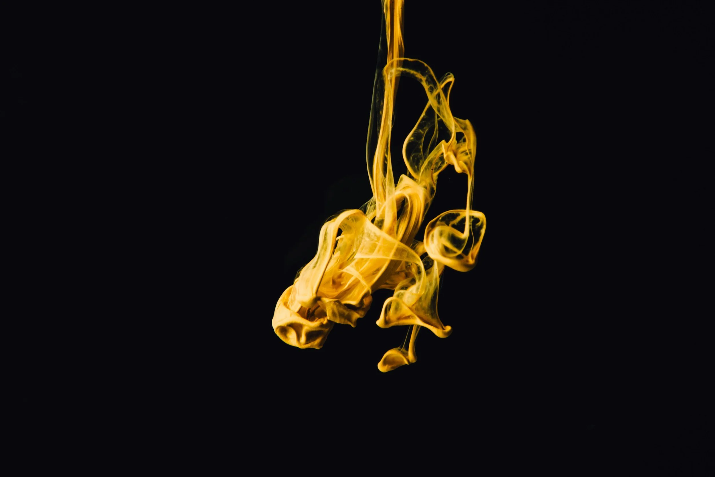 Yellow ink swirling in black background creating abstract patterns.